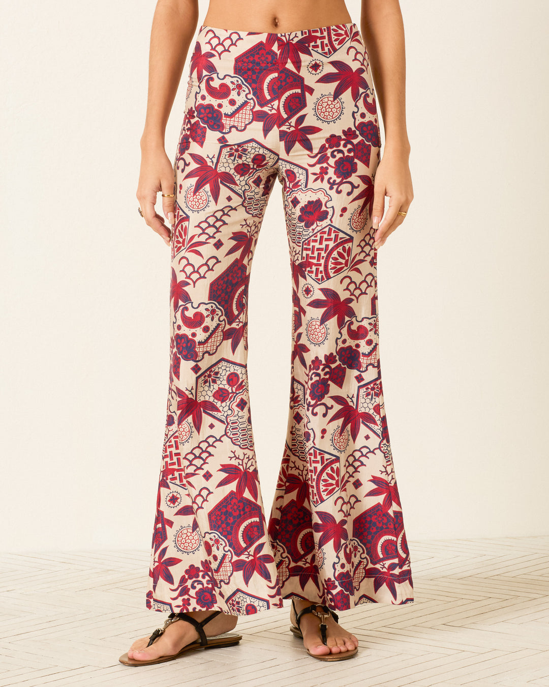 Wearing the Farah Crimson Hive Silk Pant, featuring a high-waisted, wide-leg silhouette with red and beige floral and geometric prints, paired with black sandals.