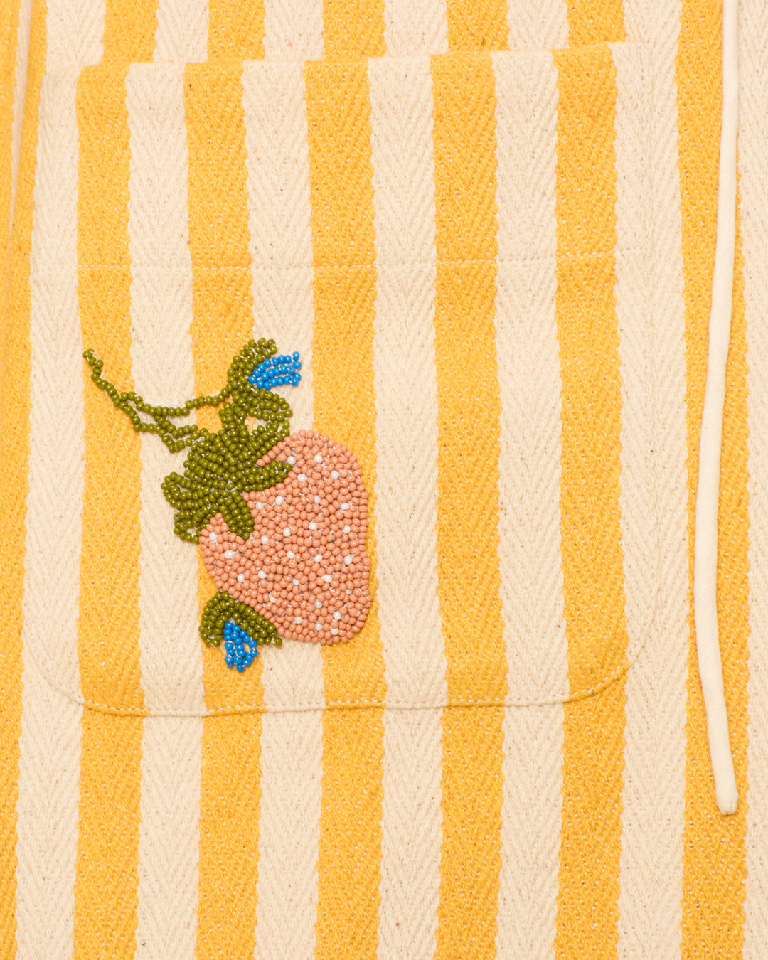 The Isadora Sunlight Stripe Dress features yellow and white stripes, crafted from cotton twill with a hand-beaded strawberry accent on the pocket.