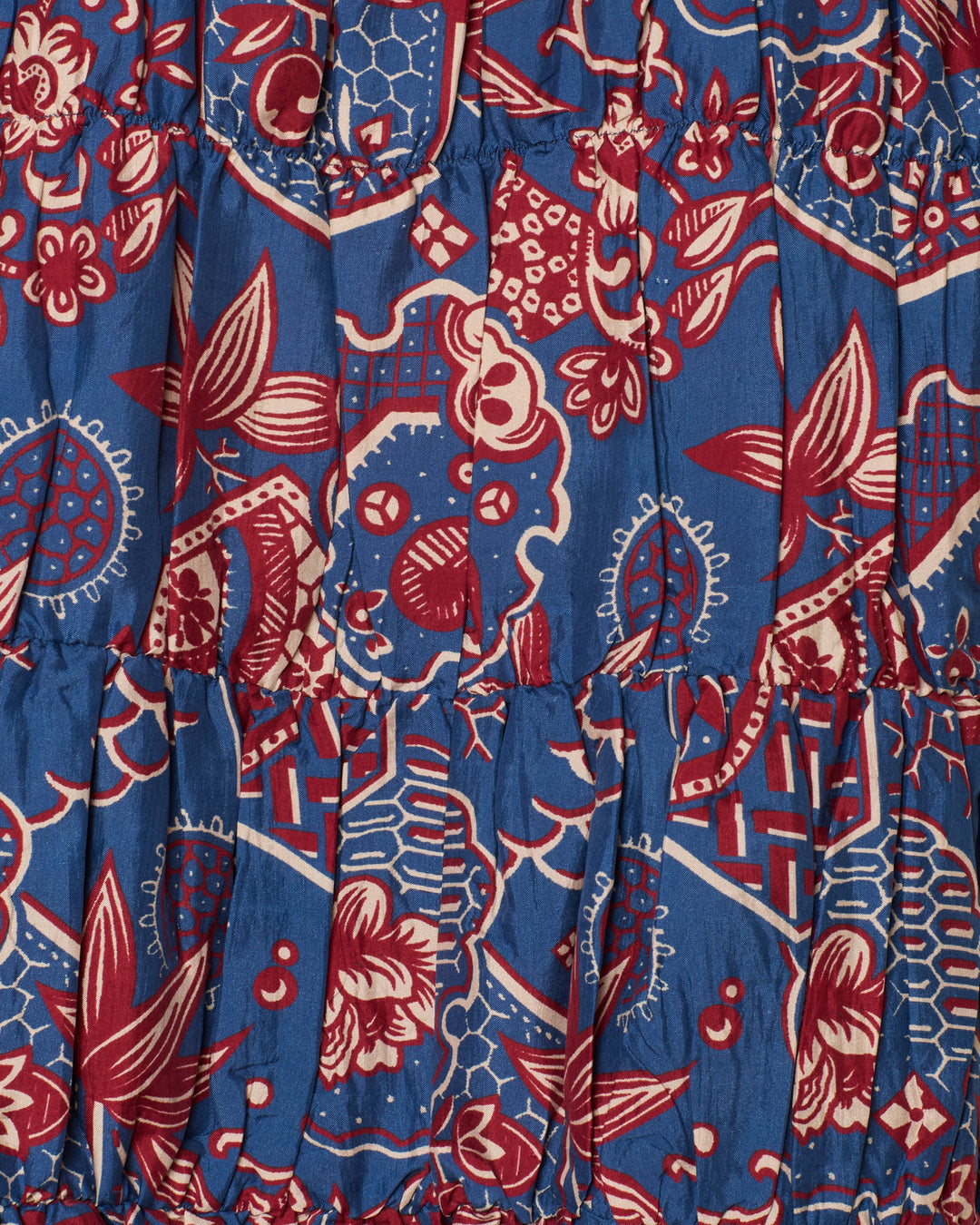 Close-up of the Jule Delft Hive Silk Dress, featuring vibrant abstract floral and geometric patterns in red, white, and blue reminiscent of a wagara print, with ruffled horizontal seams.