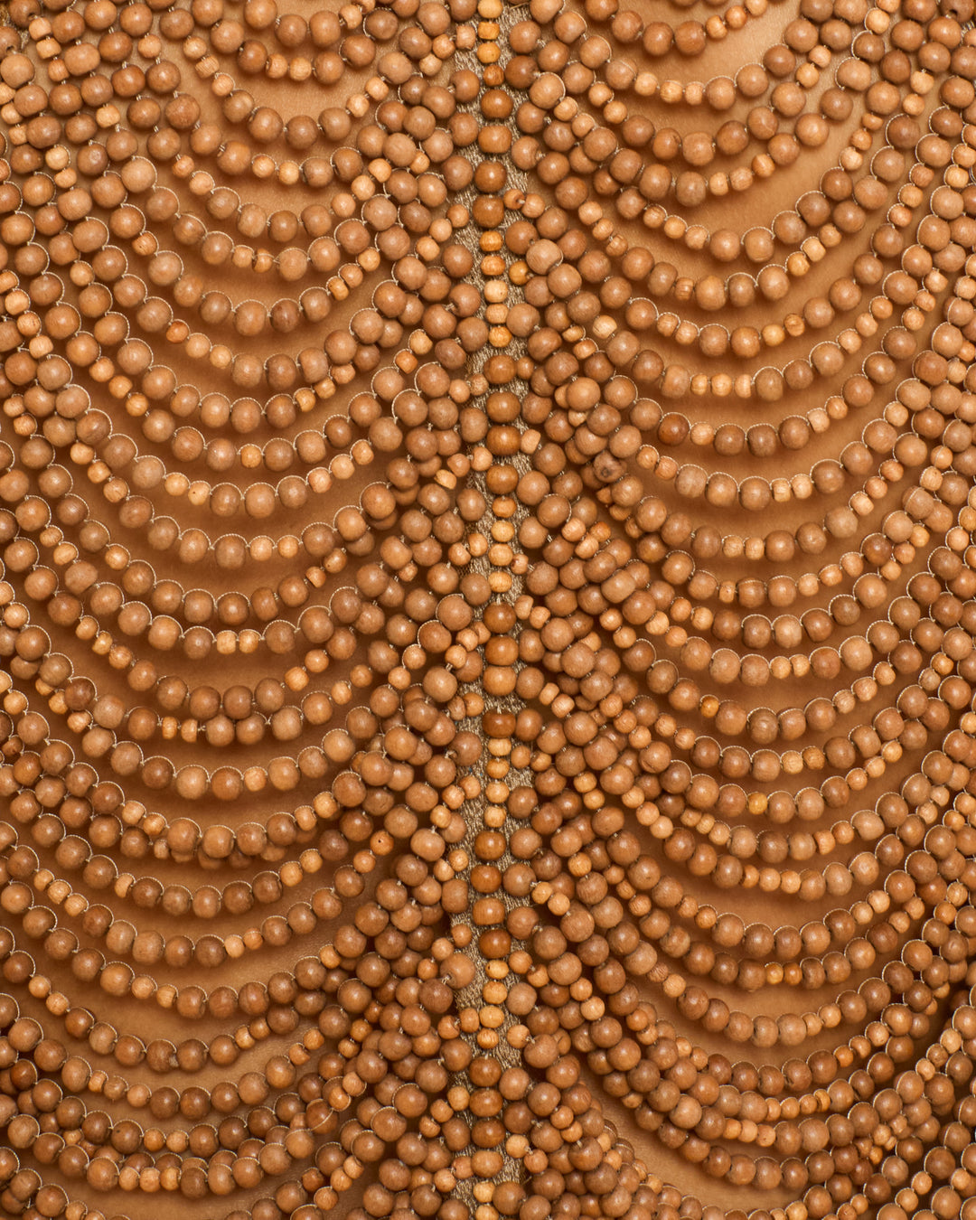 Symmetrical rows of round wooden beads form the Lania Fawn Wood Top, handmade by artisans and draping elegantly against a brown background.