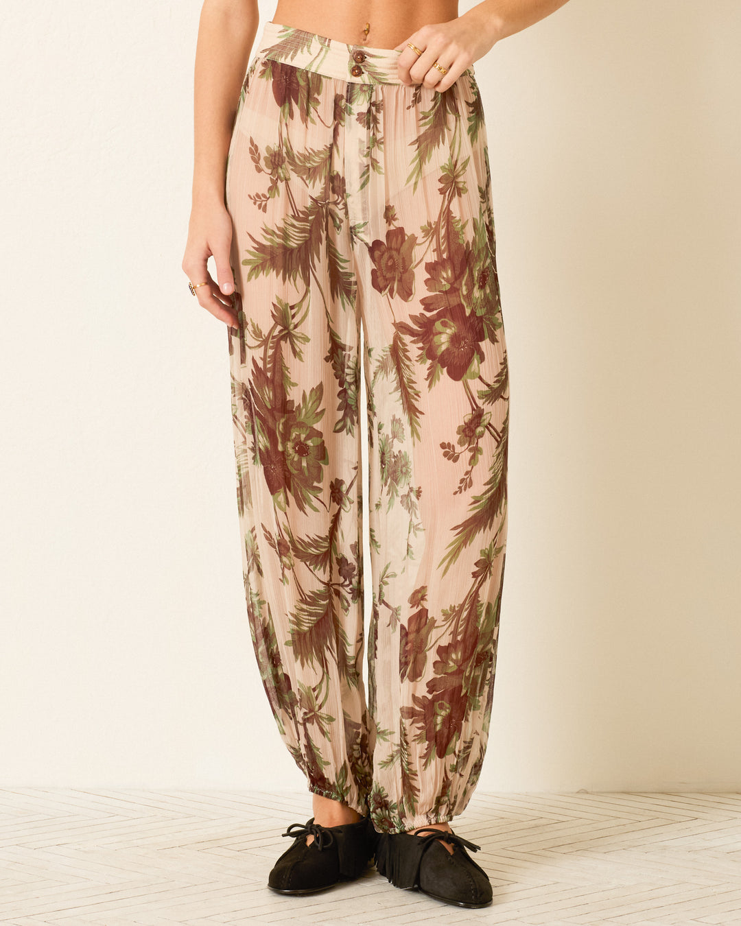 Wearing the Margot Summermoss Pant—high-waisted, harem-style cupro-chiffon pants in a brown botanical print on pink, gathered at the ankles and paired with black shoes.