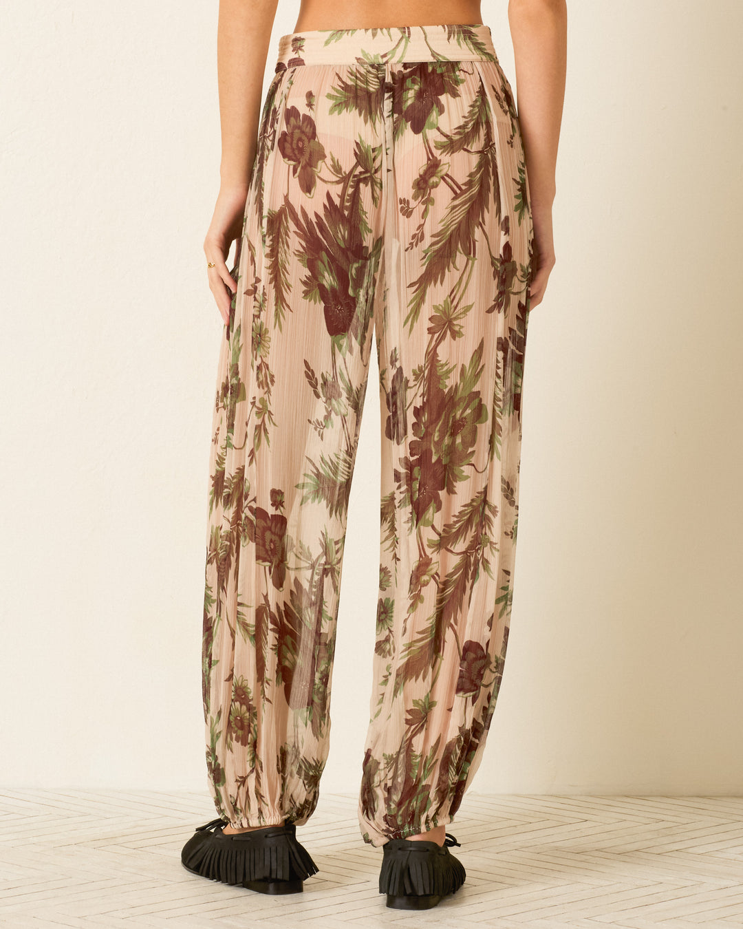A person shown from the back wears the Margot Summermoss Pant—loose harem-style pants with a botanical motif and gathered ankles—paired with black shoes against a neutral background.
