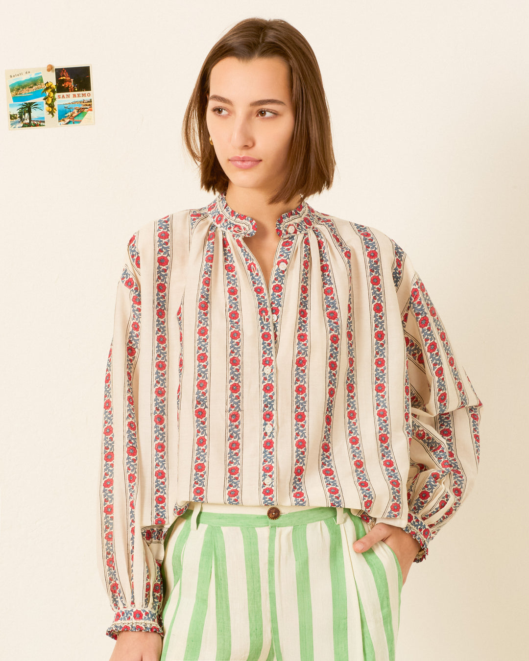 A person wearing the Poet Roseband Stripe Blouse with green and white striped pants stands against a light wall adorned with small photos in the background.