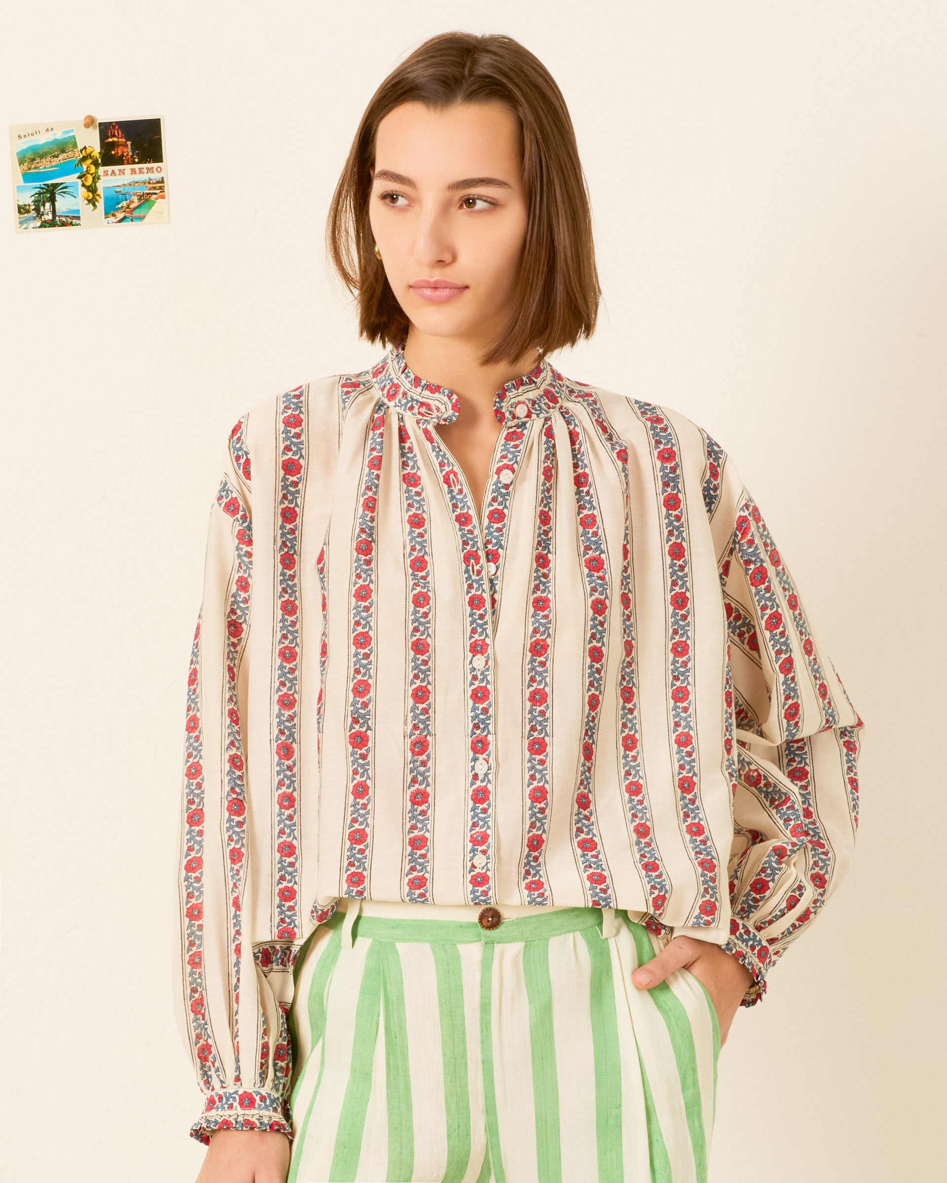 A person wearing the Poet Roseband Stripe Blouse with green and white striped pants stands against a light wall adorned with small photos in the background.