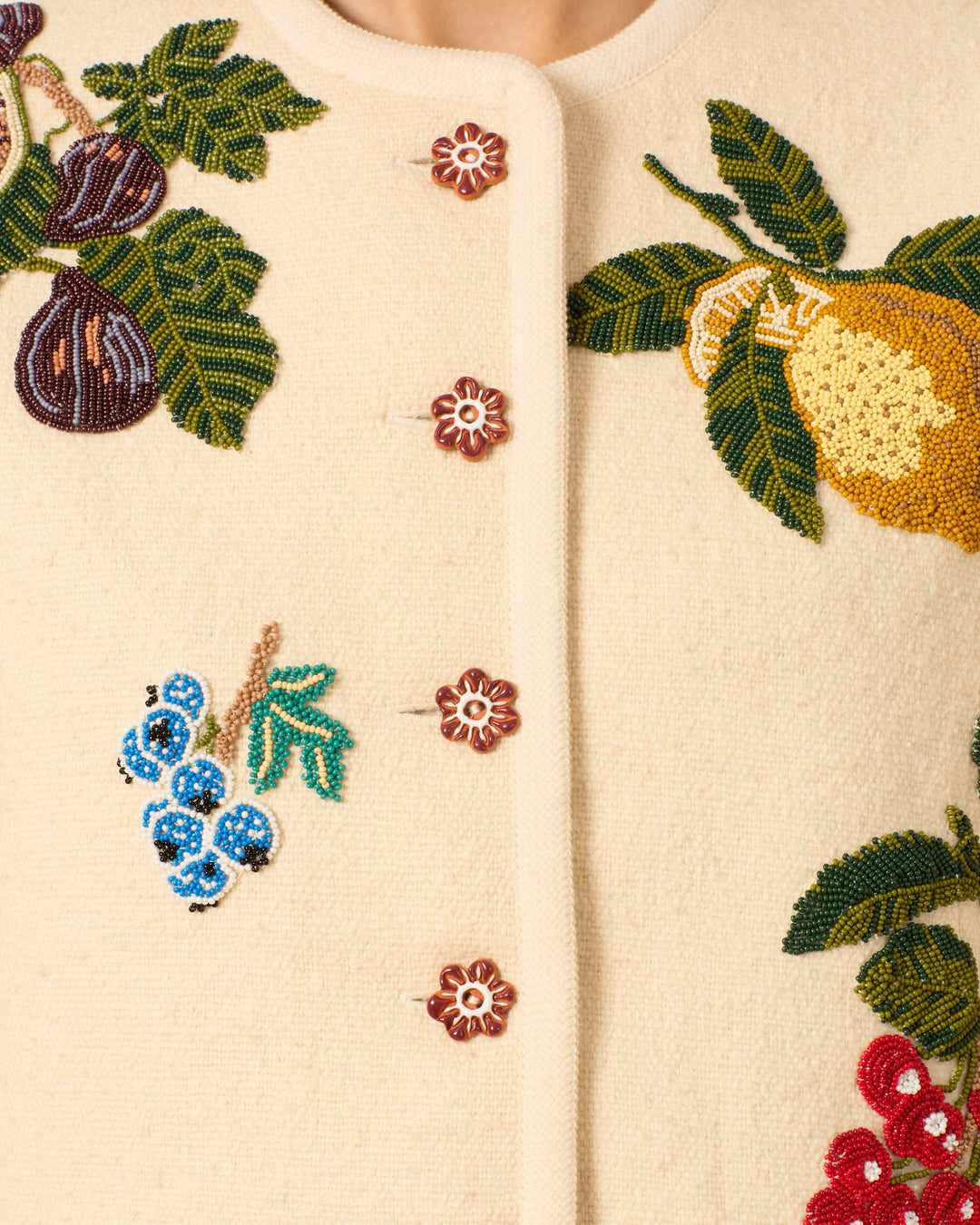 Close-up of the Rowan Nine Fruit Bead Jacket—a cream Khadi cotton piece featuring floral buttons and beaded fruit motifs like figs, grapes, blueberries, lemons, and leaves inspired by an Italian summer.