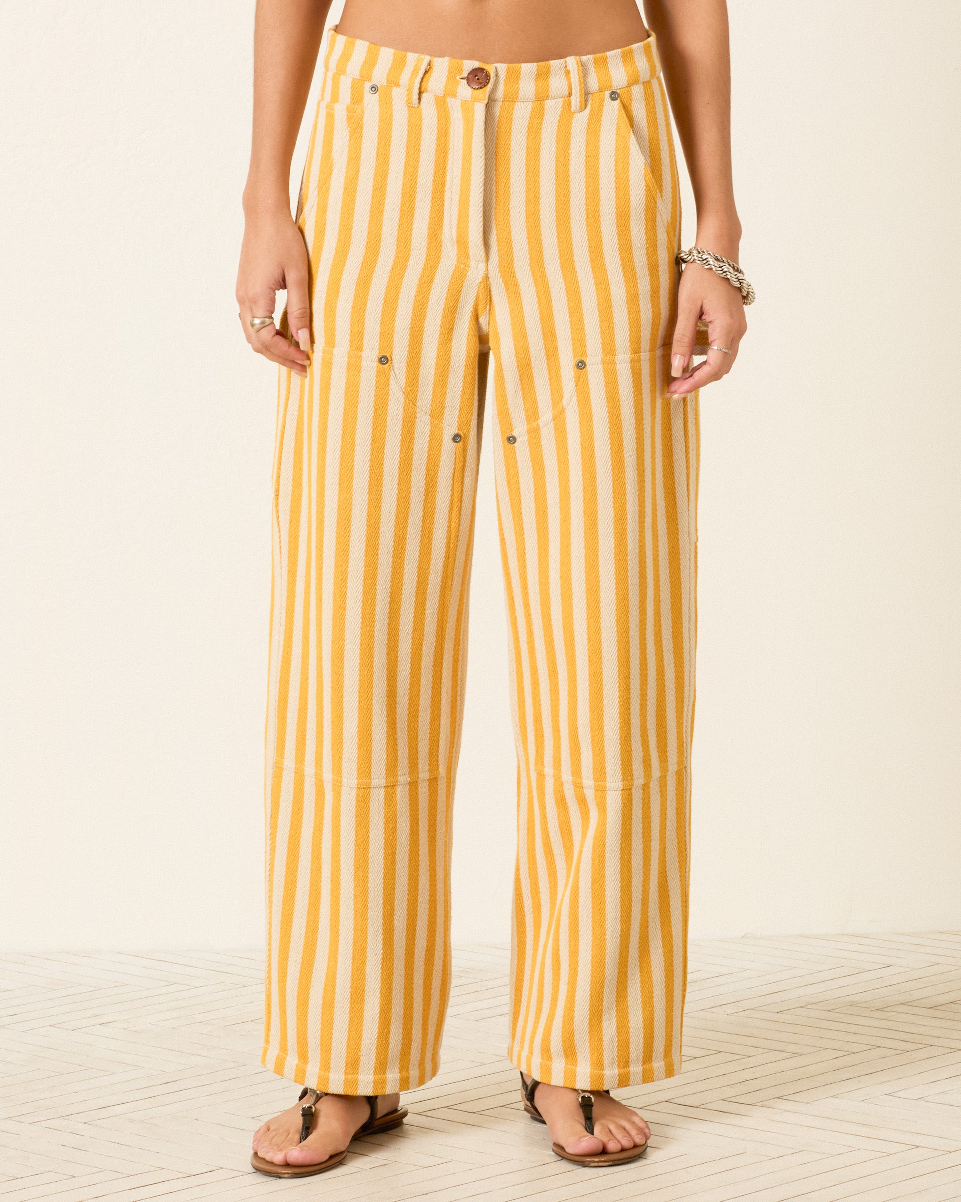 Woman wearing the Scottie Sunlight Stripe Pant in yellow and white vertical stripes, high-rise and straight-leg, shown from waist to feet standing on a light patterned floor.