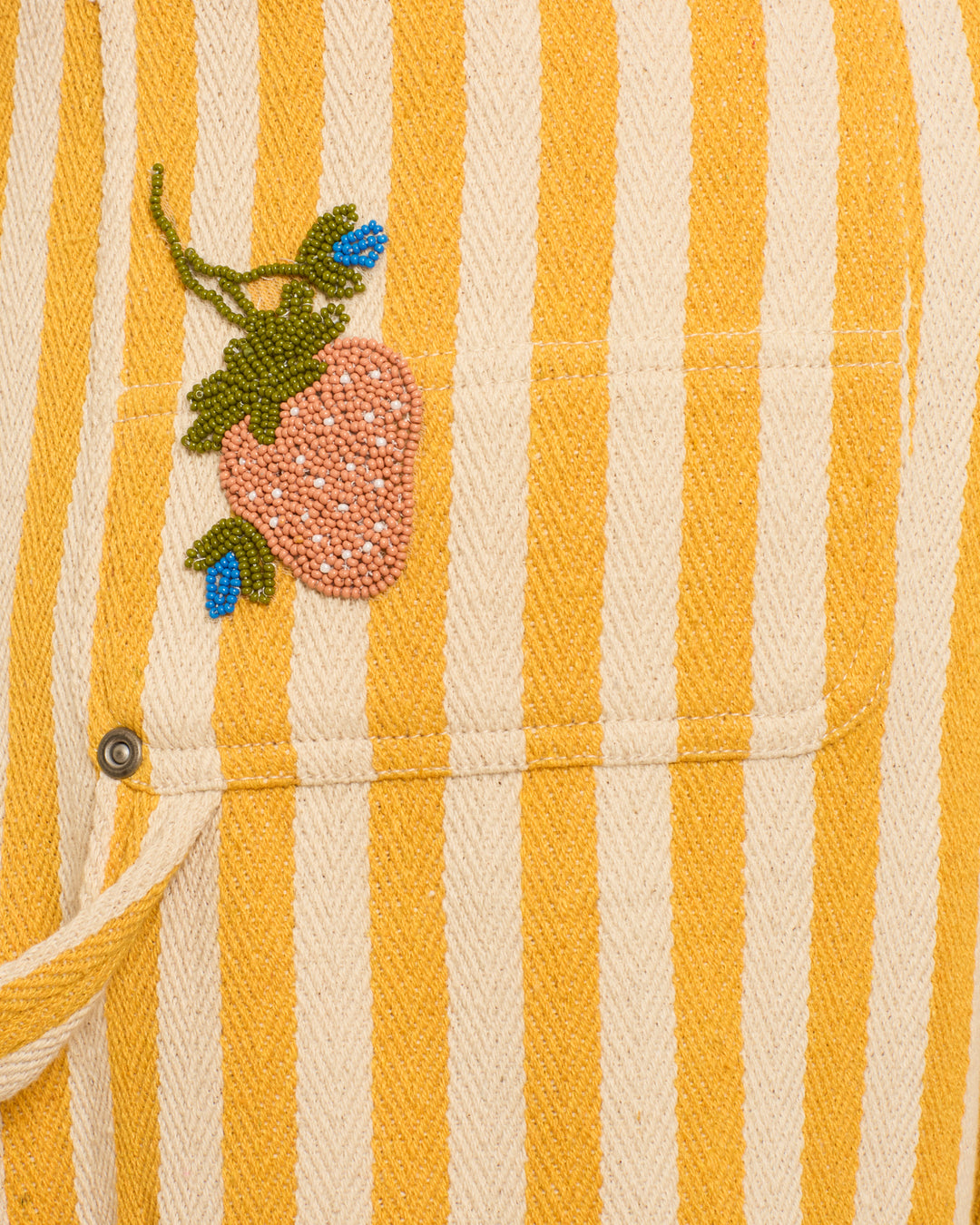 The Scottie Sunlight Stripe Pant features yellow and white stripes with a hand-beaded pink strawberry and blue leaves embroidered above the pocket, adding playful charm.