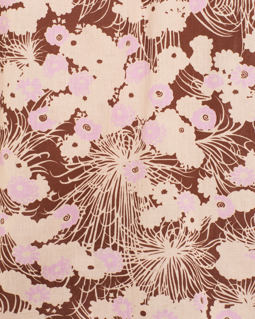The Winnie Dandelion Dusk Shirt showcases patterned fabric with abstract floral shapes in light pink and beige on a brown background, accented by swirling and radiating lines—ideal for its cotton voile construction with a ruffled collar or softly gathered puff shoulders.