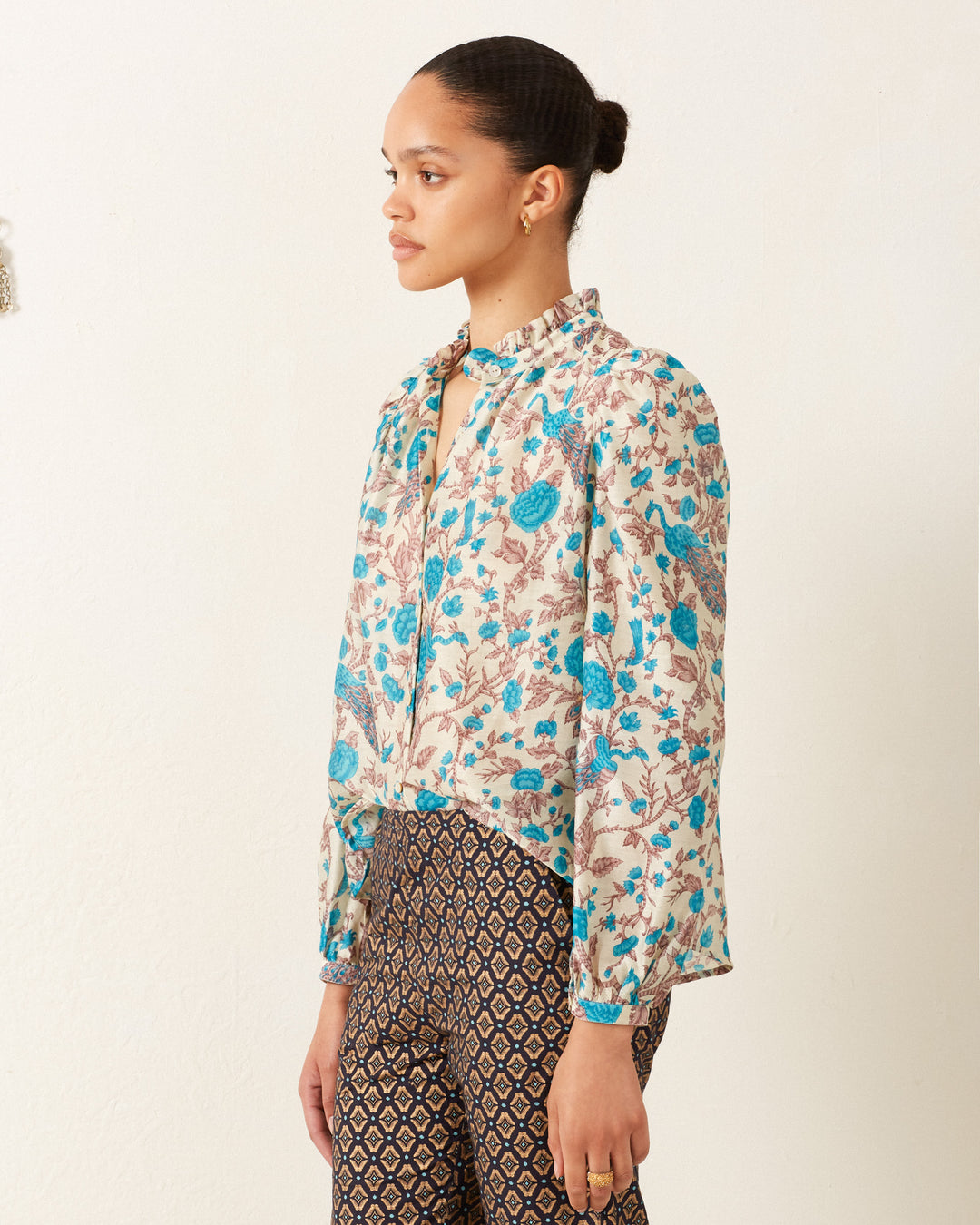 A person wearing the Annabel Peacock Plume Shirt and patterned pants stands against a plain background, looking to the side.