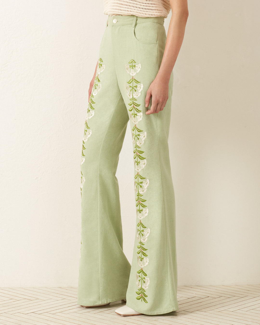 A person wearing light green wide-leg Bunny Trumpet Love Jean pants with a '70s vibe, featuring white and green floral embroidery.