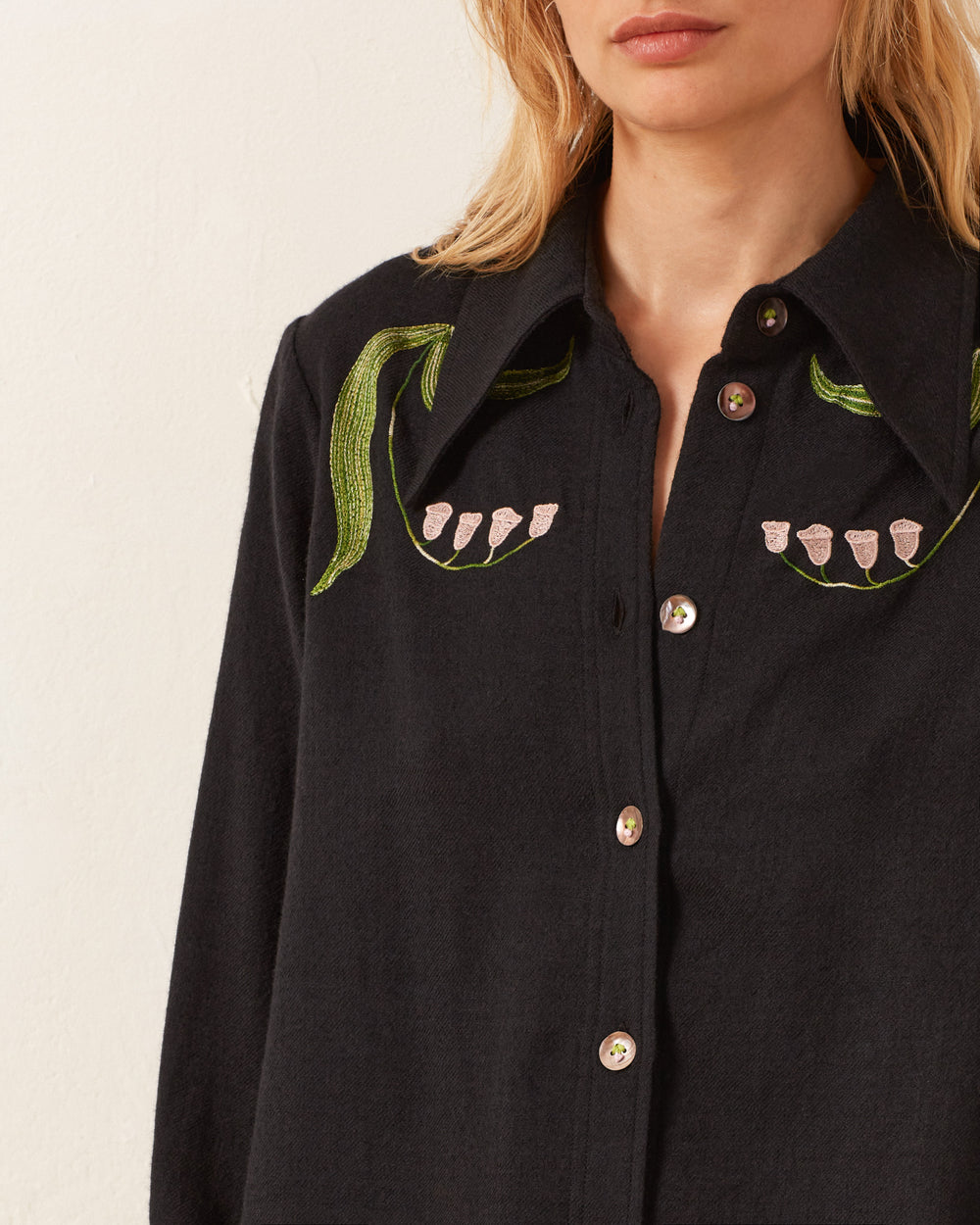 A person wearing the Dolly Lily Valley Shirt, a black button-up with vintage-inspired floral embroidery near the shoulders.