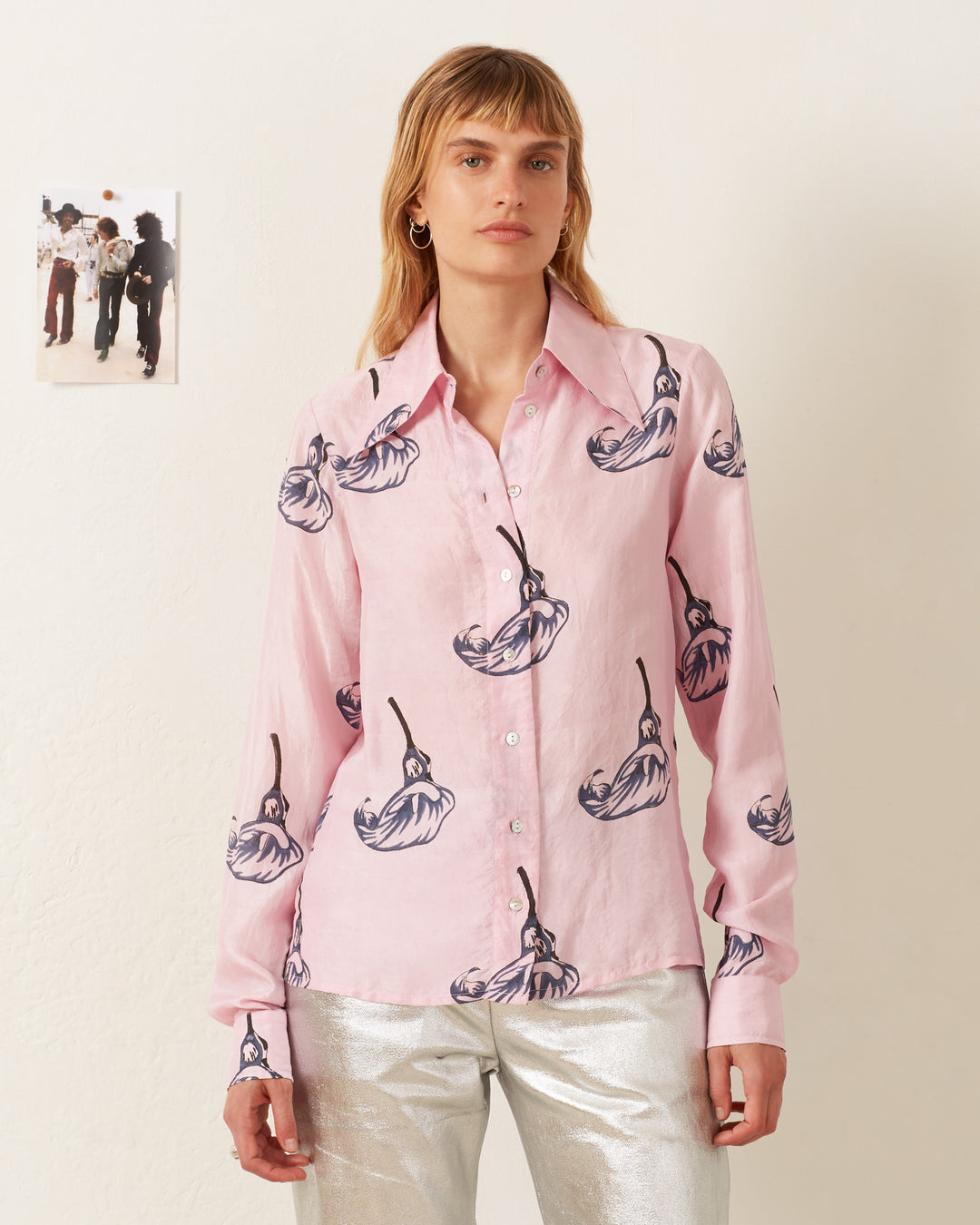 Person wearing a Dolly Pink Calla Lily Shirt, paired with metallic silver pants, standing indoors next to a small photo on the wall.