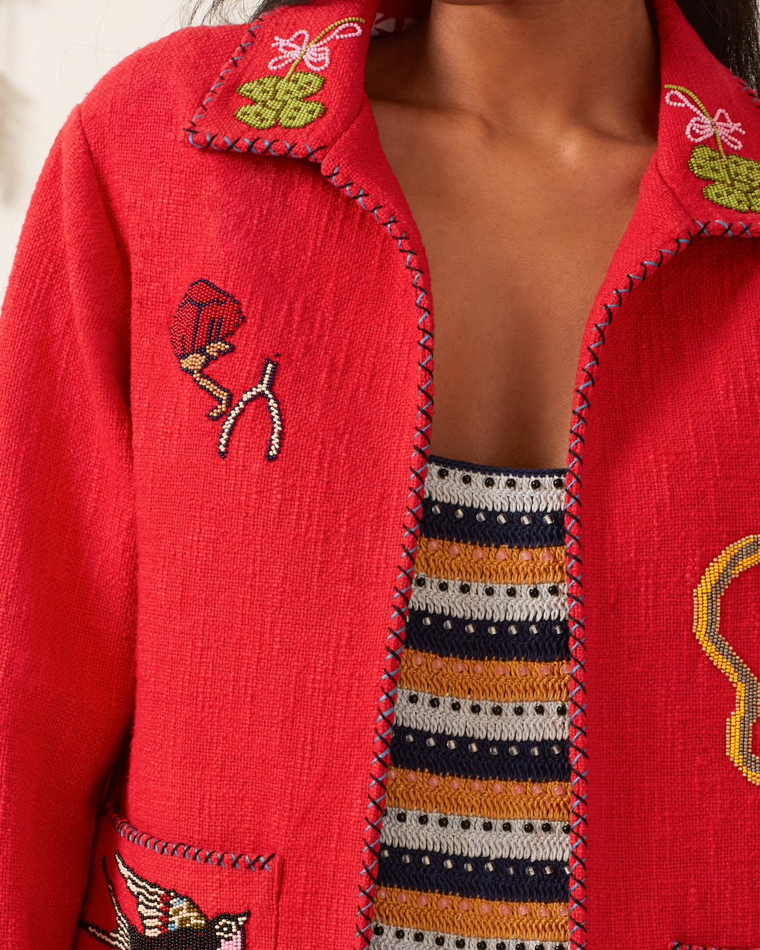 Close-up of a person wearing the Francis Crimson Tattoo Jacket, showcasing intricate embroidery and detailed stitching that exudes a vintage charm, perfectly complementing the striped top underneath.