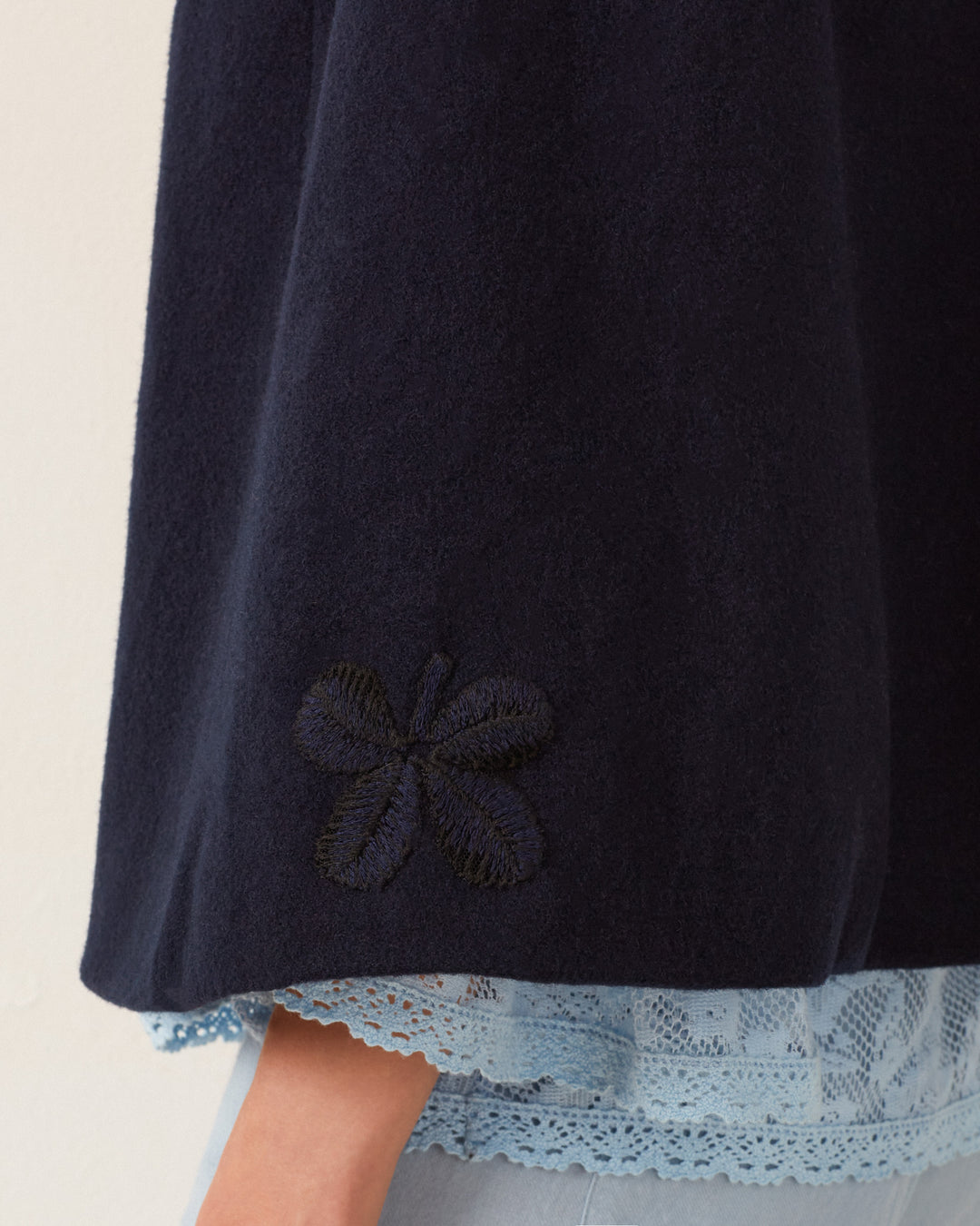 Close-up of the Kensington Midnight Wool Cape, featuring a dark blue color with subtle butterfly embroidery near the hem, layered over light blue lace detail.