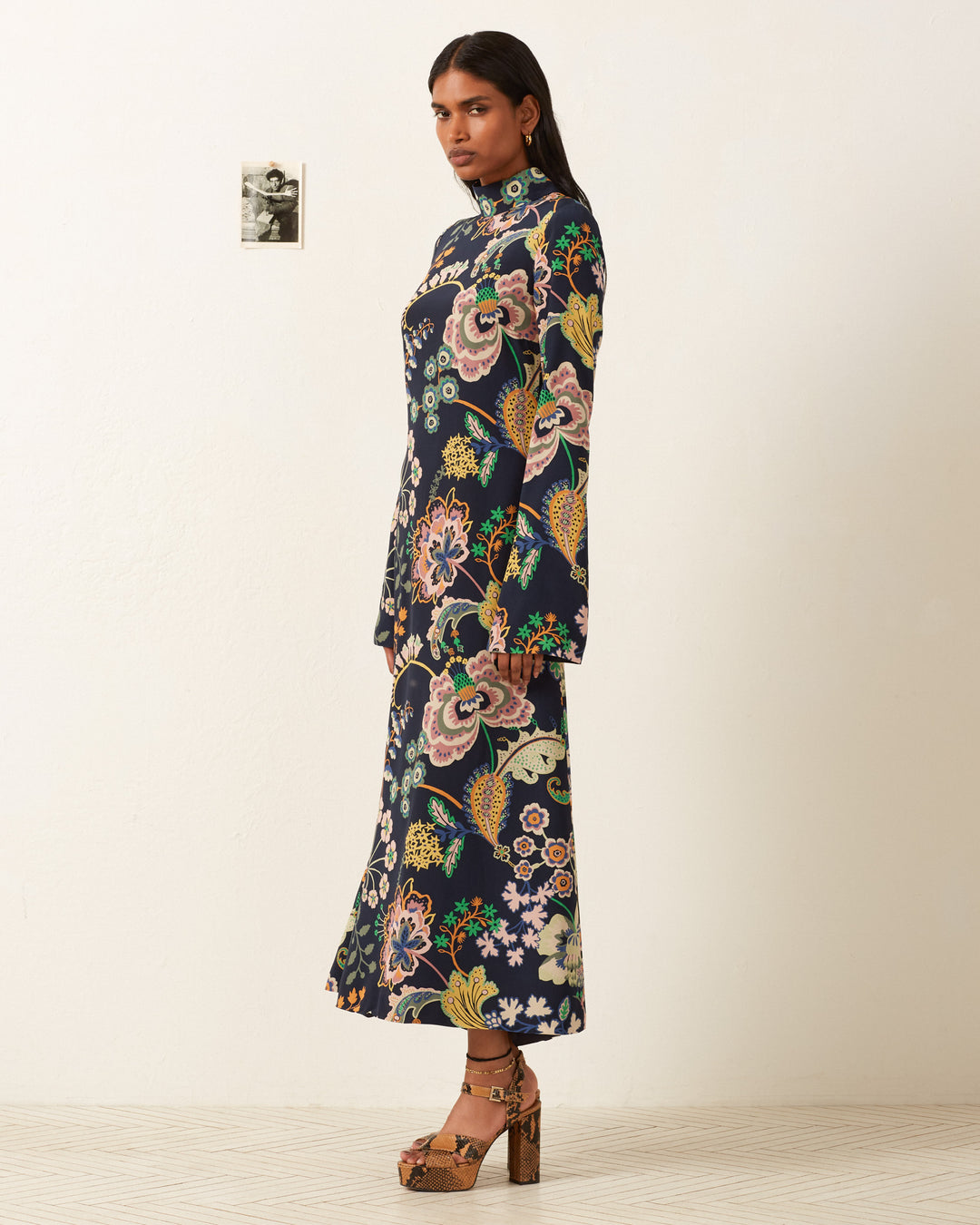 In a minimalist room with a small photo on the wall, a person is wearing the Nia Desert Flower Dress.