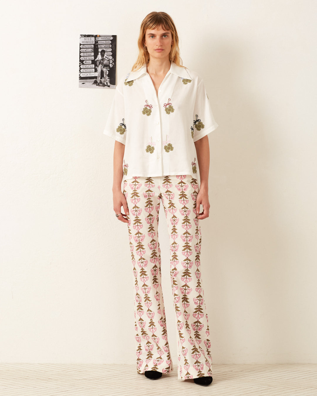 A person wearing the Stevie Lucky Clover Shirt and patterned Tencel wide-leg pants stands against a white wall, with a small poster displayed beside them.