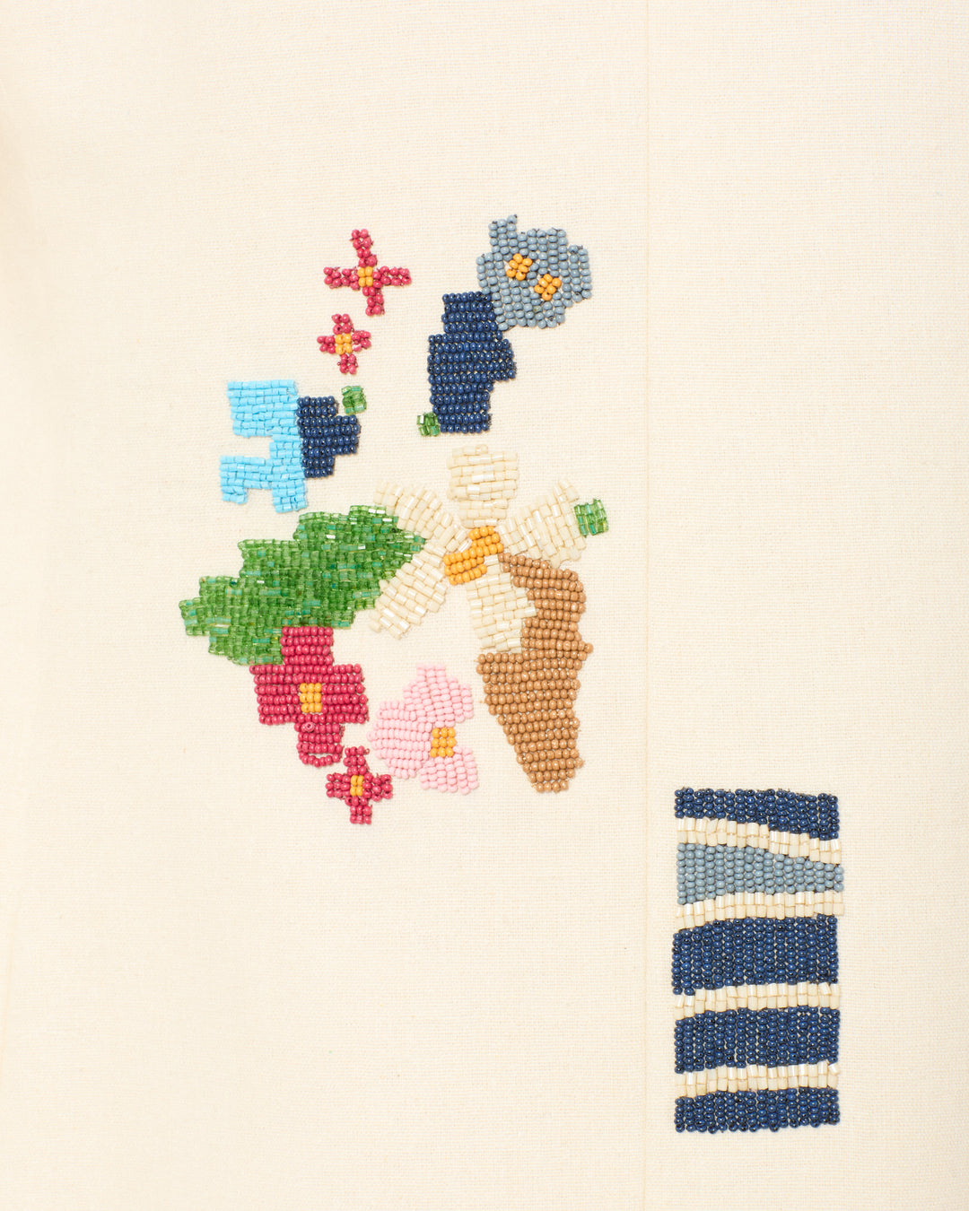 The Afternoon Abstract Tile Blazer is a cream-colored piece adorned with colorful abstract floral embroidery and a blue-and-white striped detail at the bottom right.