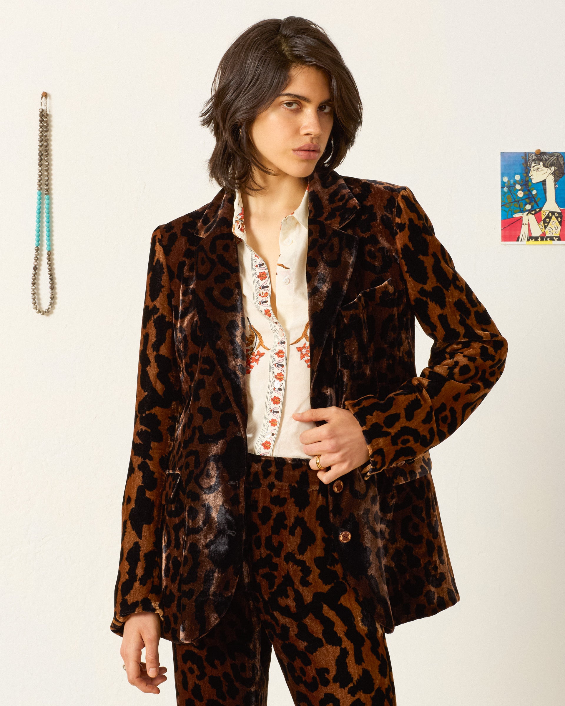 Wearing the Afternoon Leopard Blazer in brown and black with a white embroidered shirt, this person stands indoors against a plain wall with minimal decorations.