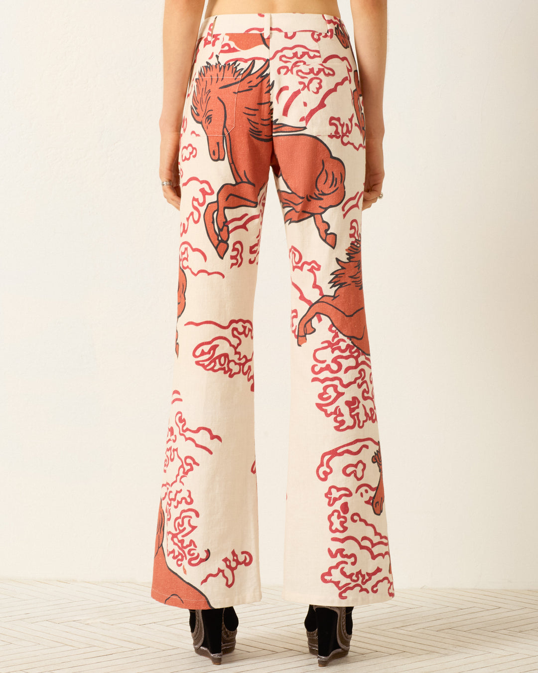 Person wearing Bunny Rouge Pegasus Jean, cream-colored wide-leg khadi cotton pants featuring a red horse and cloud print plus a handmade button, shown from the back against a neutral background.