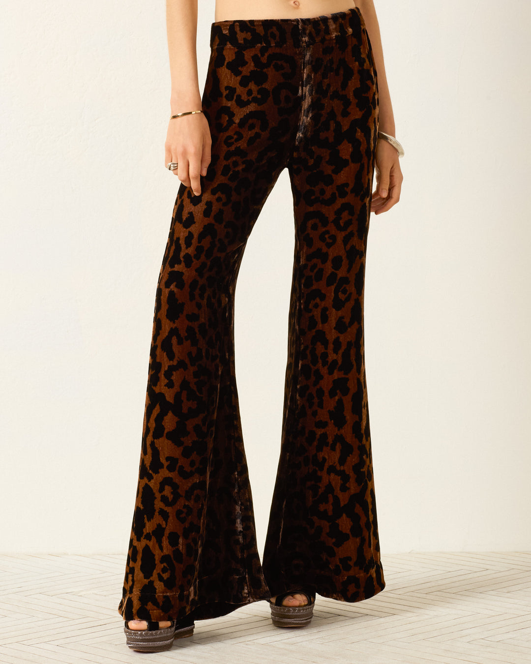 Model wears the Farah Leopard Velvet Pant, featuring a high waist and dramatic bell-bottom flare, paired with platform sandals against a plain light background.