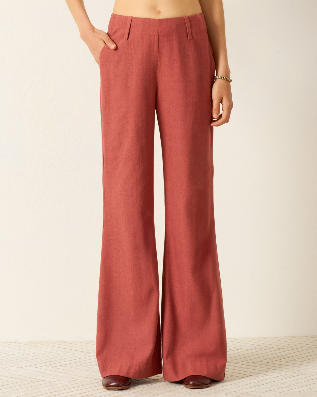 Wearing the Charlie Red Ochre Silk Pant—high-waisted, flared-leg trousers with side pockets—standing on a light patterned floor. Only the lower torso and legs are visible.