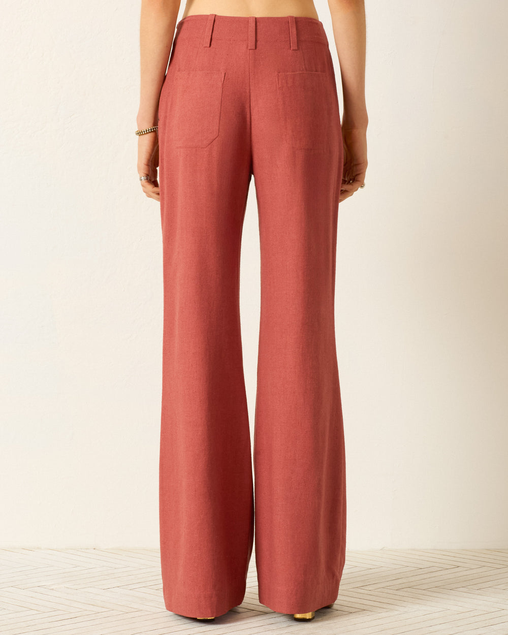 Someone is seen from behind wearing the Charlie Red Ochre Silk Pant, a high-waisted, wide-leg rust-colored silk pant, set against a light background.