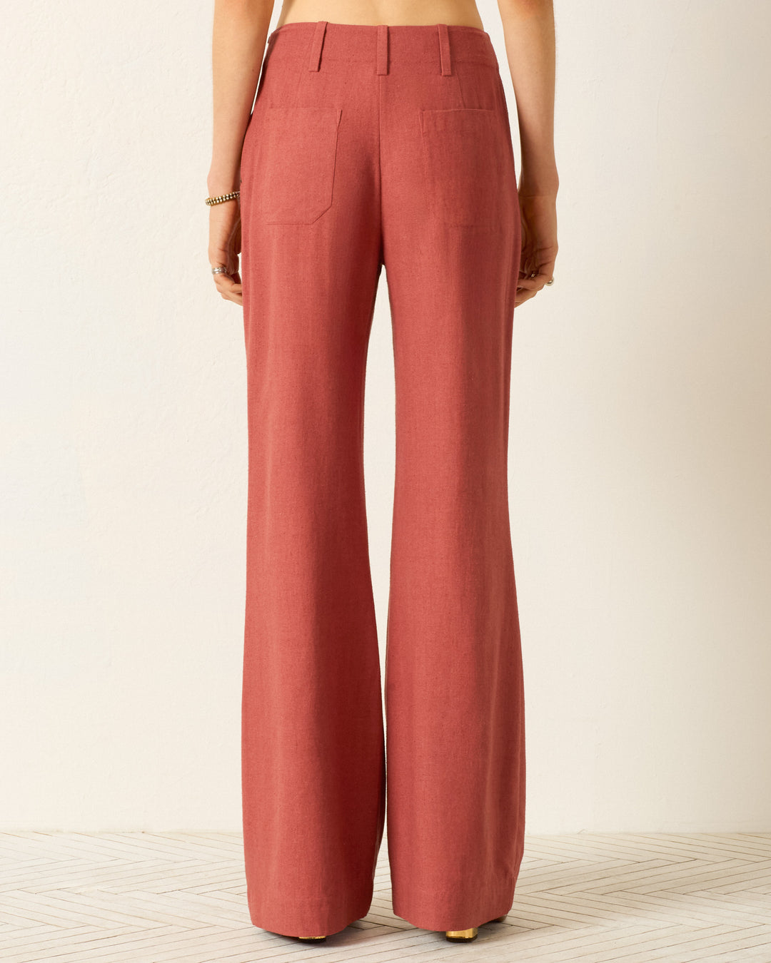 Someone is seen from behind wearing the Charlie Red Ochre Silk Pant, a high-waisted, wide-leg rust-colored silk pant, set against a light background.