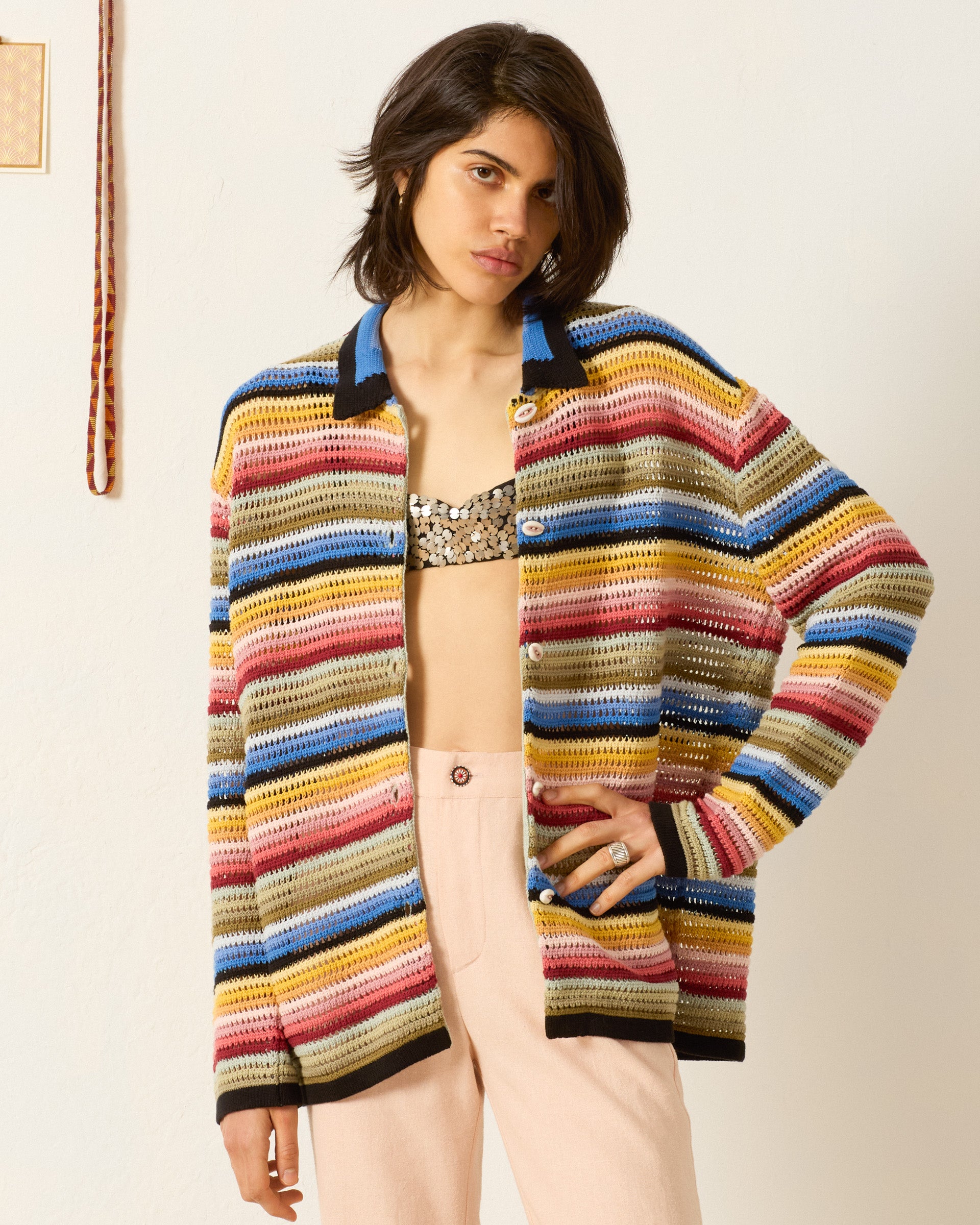 A woman wears the Emery Ombre Crochet Top over a sequined bralette and pale pink pants, standing against a plain wall.