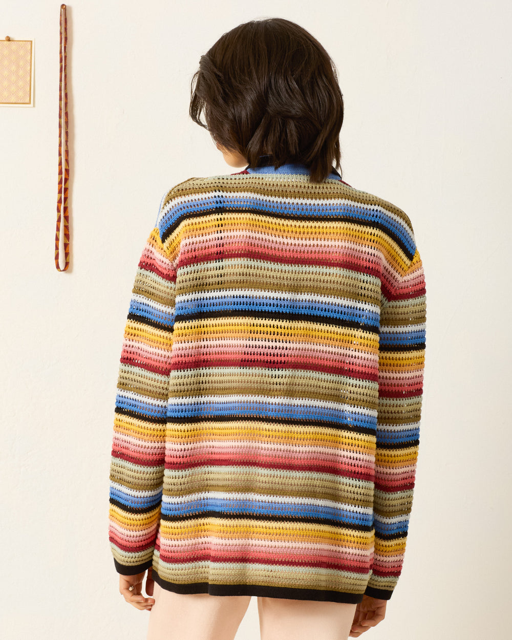 A person with short dark hair, seen from behind, wears the Emery Ombre Crochet Top against a plain wall.