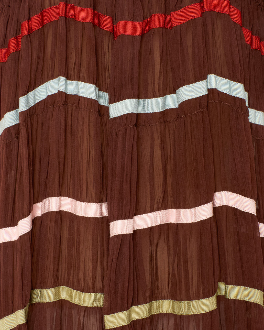 Close-up of the Emrys Clove Aurora Dress in brown pleated cupro-chiffon, featuring horizontal bands in red, light blue, pink, and green—ideal for a flowy maxi look with ruched tiers.