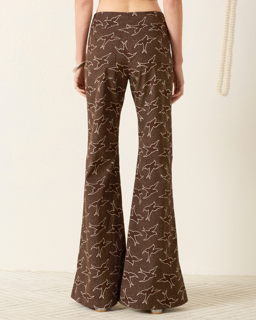 Model wears the Farah Clove Swallow Pant—brown, high-waisted with a white swallow motif—seen from the back against a plain background.