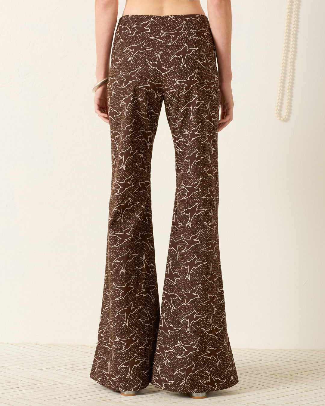 Model wears the Farah Clove Swallow Pant—brown, high-waisted with a white swallow motif—seen from the back against a plain background.