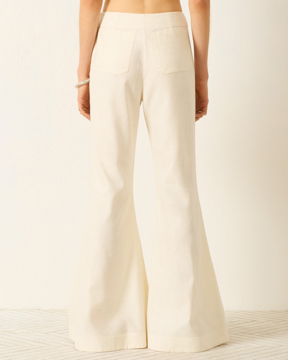 A person is seen from behind, wearing the Farah Alabaster Silk Pant—high-waisted, wide-leg cream silk pants with a subtle bell-bottom flare—against a plain light background.