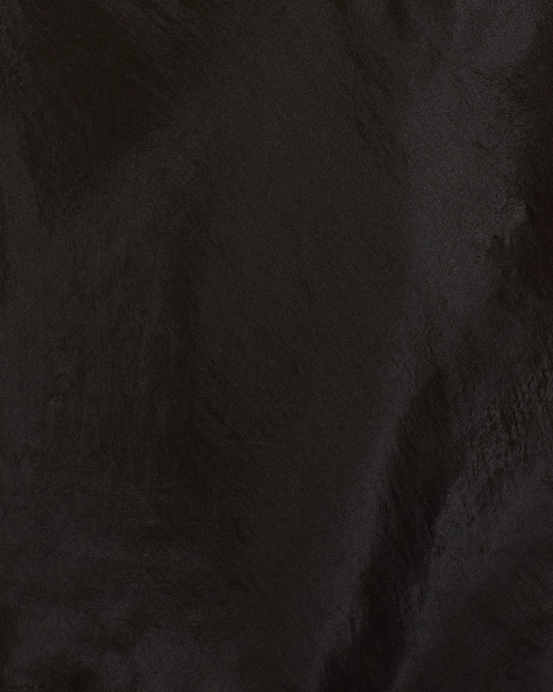 Close-up of the Fiona Gilded Coin Top’s smooth, dark black hand-loomed silk surface with subtle wavy texture and reflective highlights.