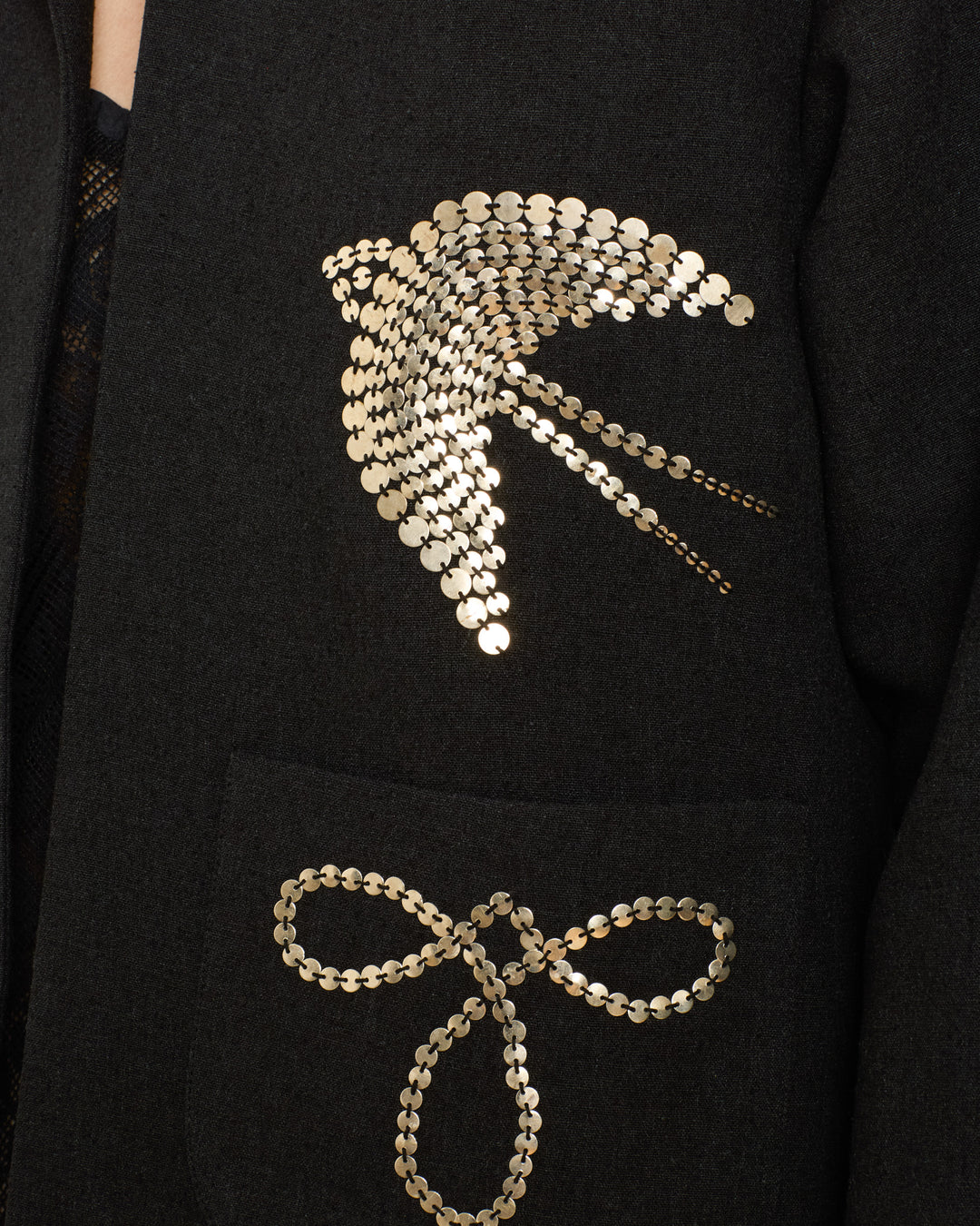 A close-up of the Francis Lovebird Coin Jacket shows its dark textured silk, a gold sequin bird above the pocket, and hand-embellished gold sequin bow with Klimt-inspired motifs.