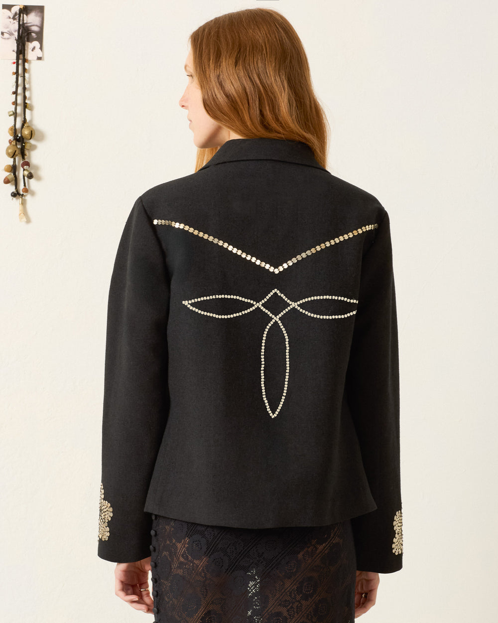 A woman with long reddish hair faces away, wearing the Francis Lovebird Coin Jacket, a textured silk piece featuring a geometric pearl pattern and hand-embellished pearls on the sleeves.