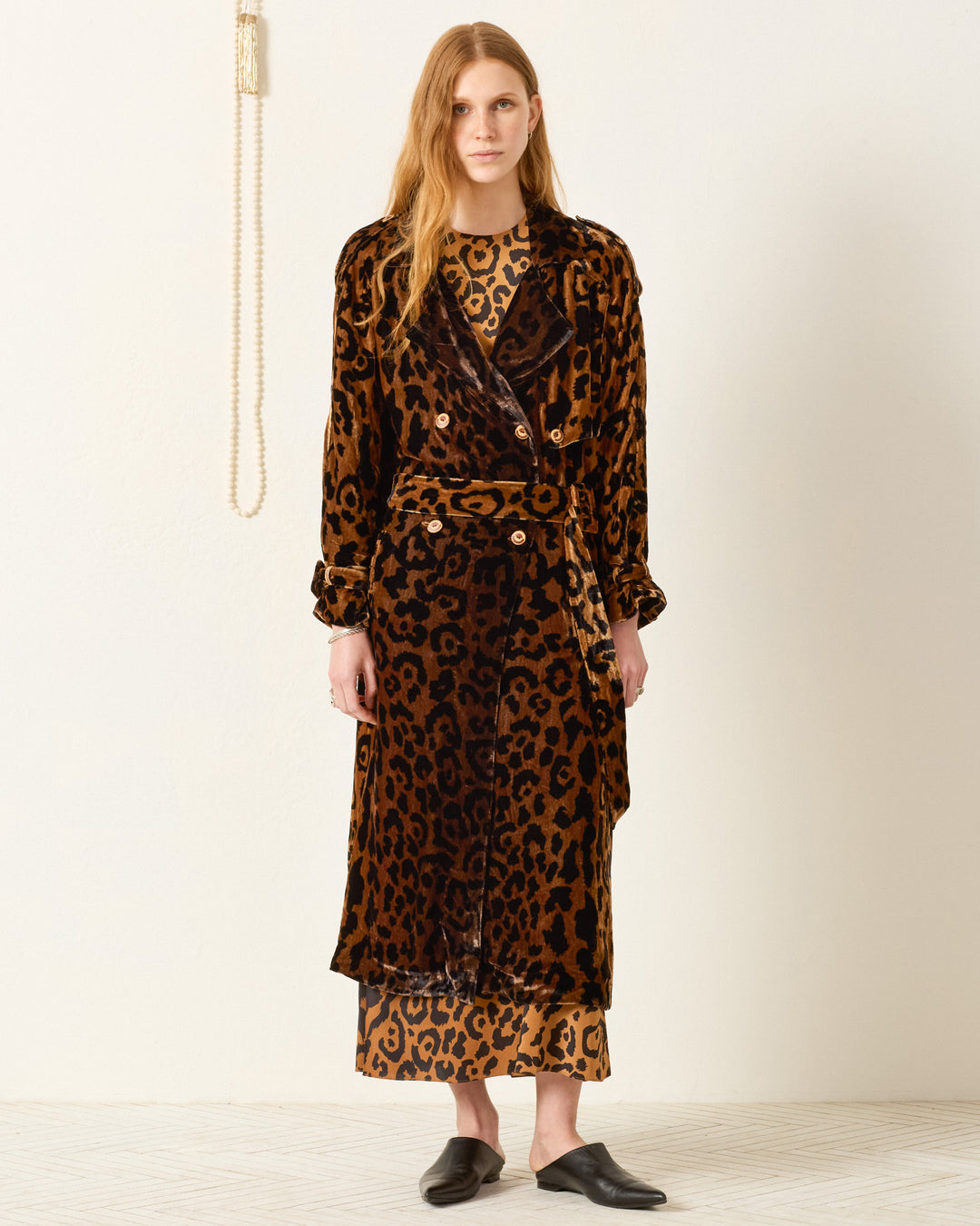 A woman stands indoors wearing the Jasper Leopard Velvet Coat over a matching dress with black slip-on shoes.