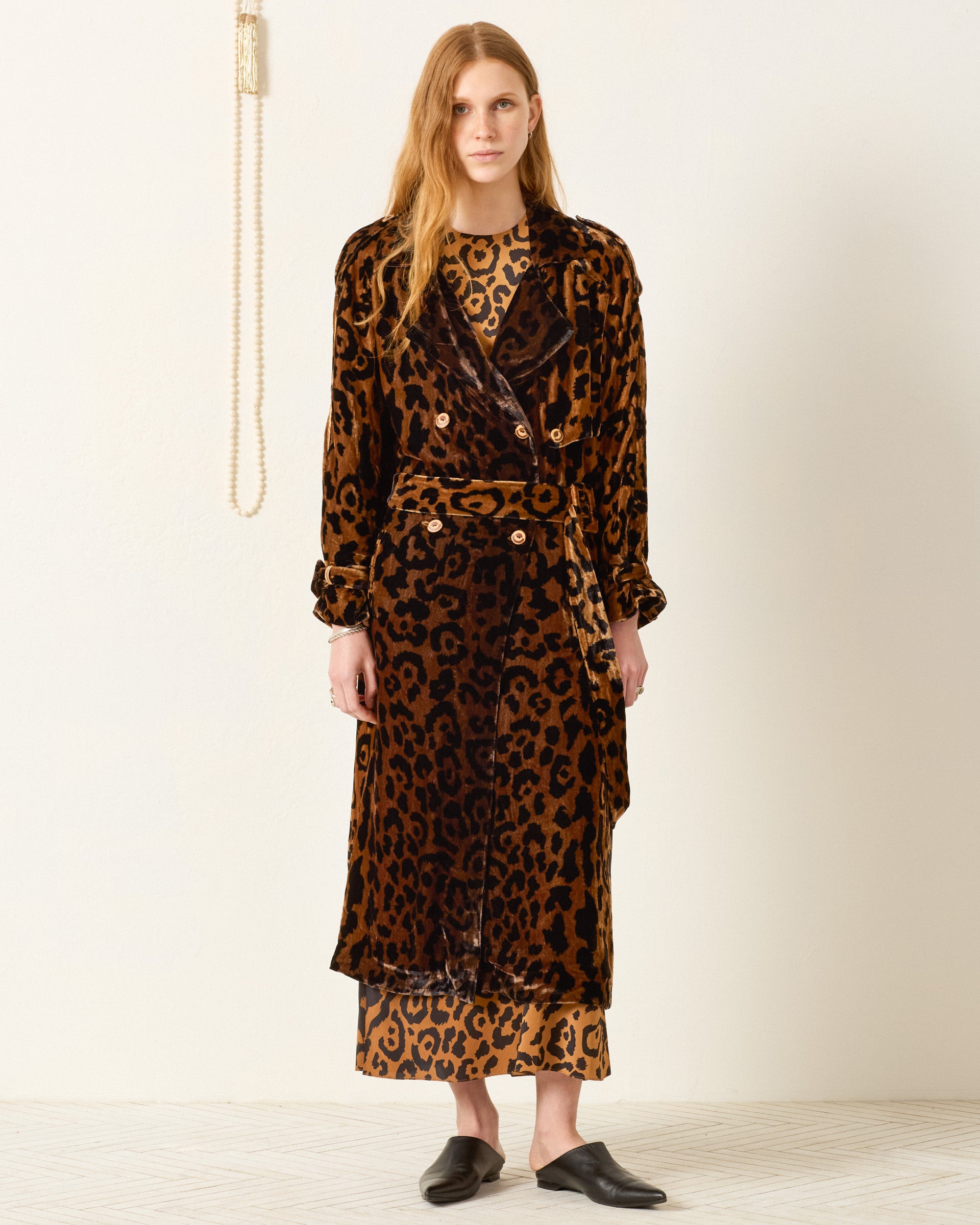 A woman stands indoors wearing the Jasper Leopard Velvet Coat over a matching dress with black slip-on shoes.
