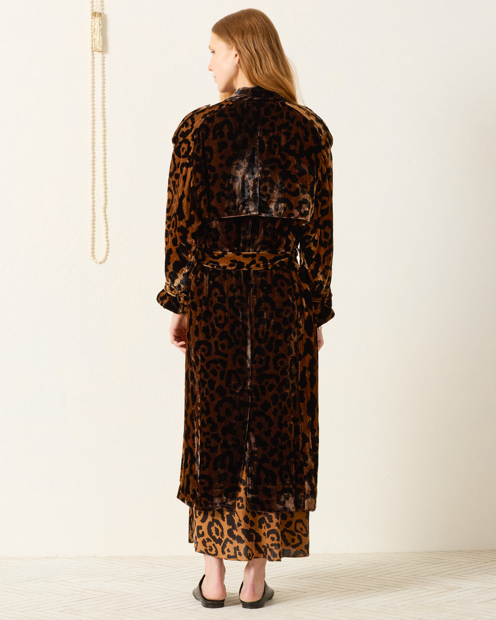 A person with long hair stands facing away, wearing the Jasper Leopard Velvet Coat over a matching dress and black sandals.