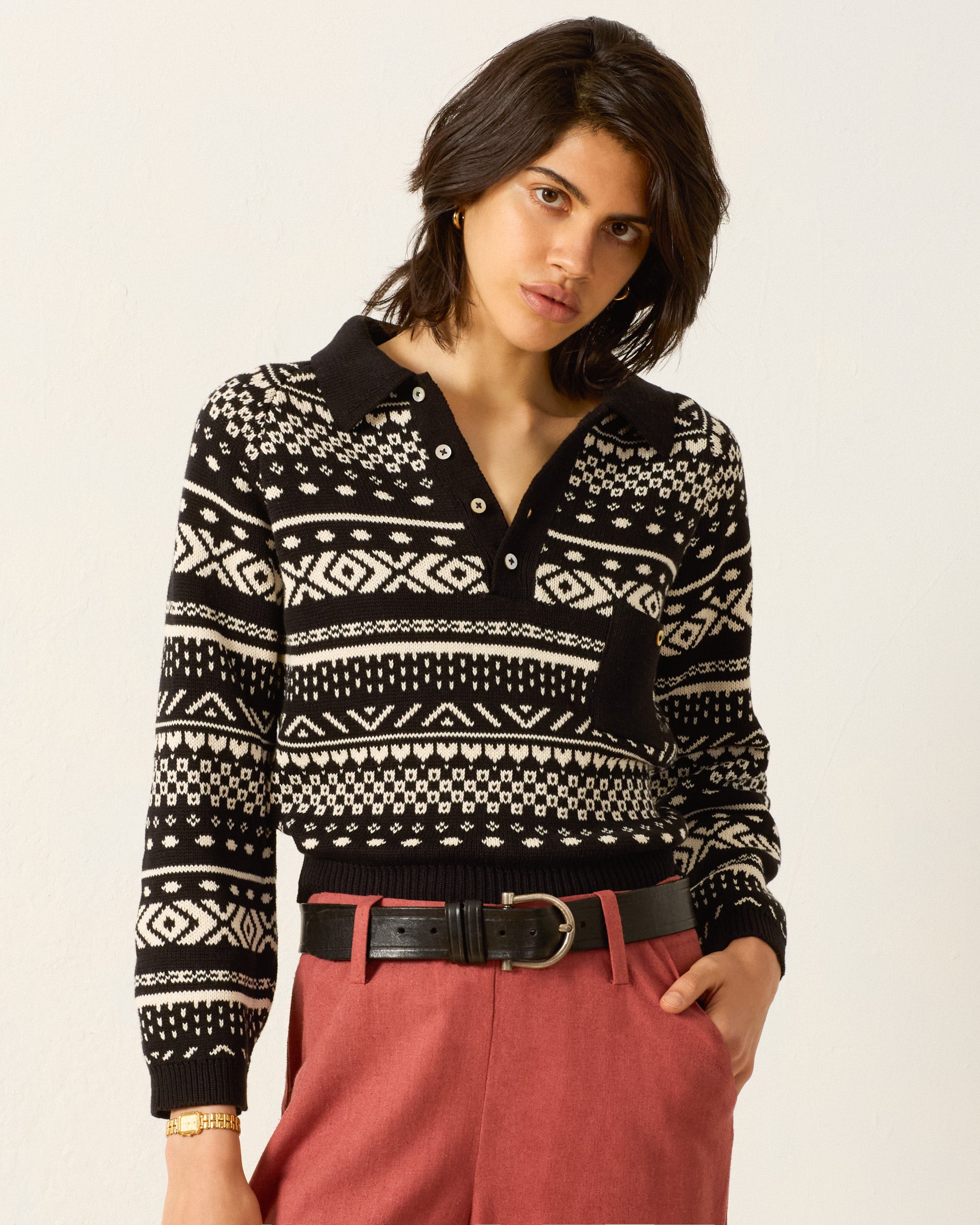 A person wearing the Liza Black Marble Top with red pants, a black belt, and a gold wristwatch stands against a plain light background.