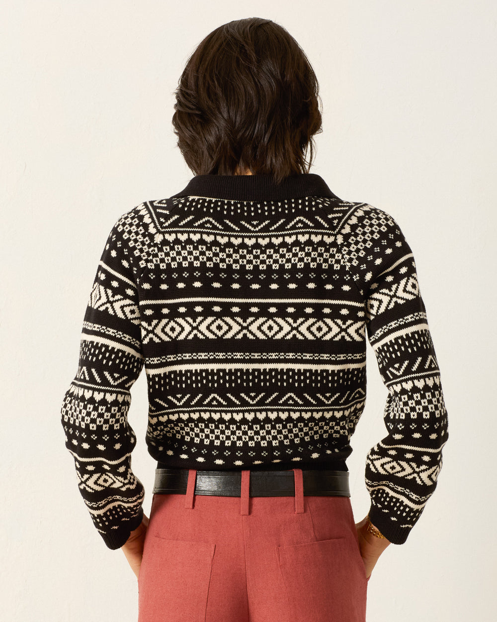 Person standing with their back to the camera, wearing the Liza Black Marble Top paired with high-waisted red trousers and a black belt.