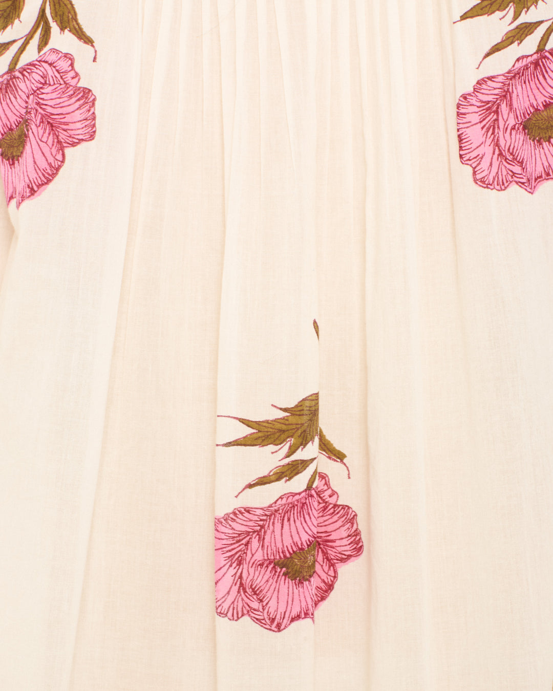 Close-up of the Nyxe Fuchsia Poppy Dress, a light beige cotton voile shirt dress adorned with hand-block-printed pink poppy flowers and green stems and leaves.