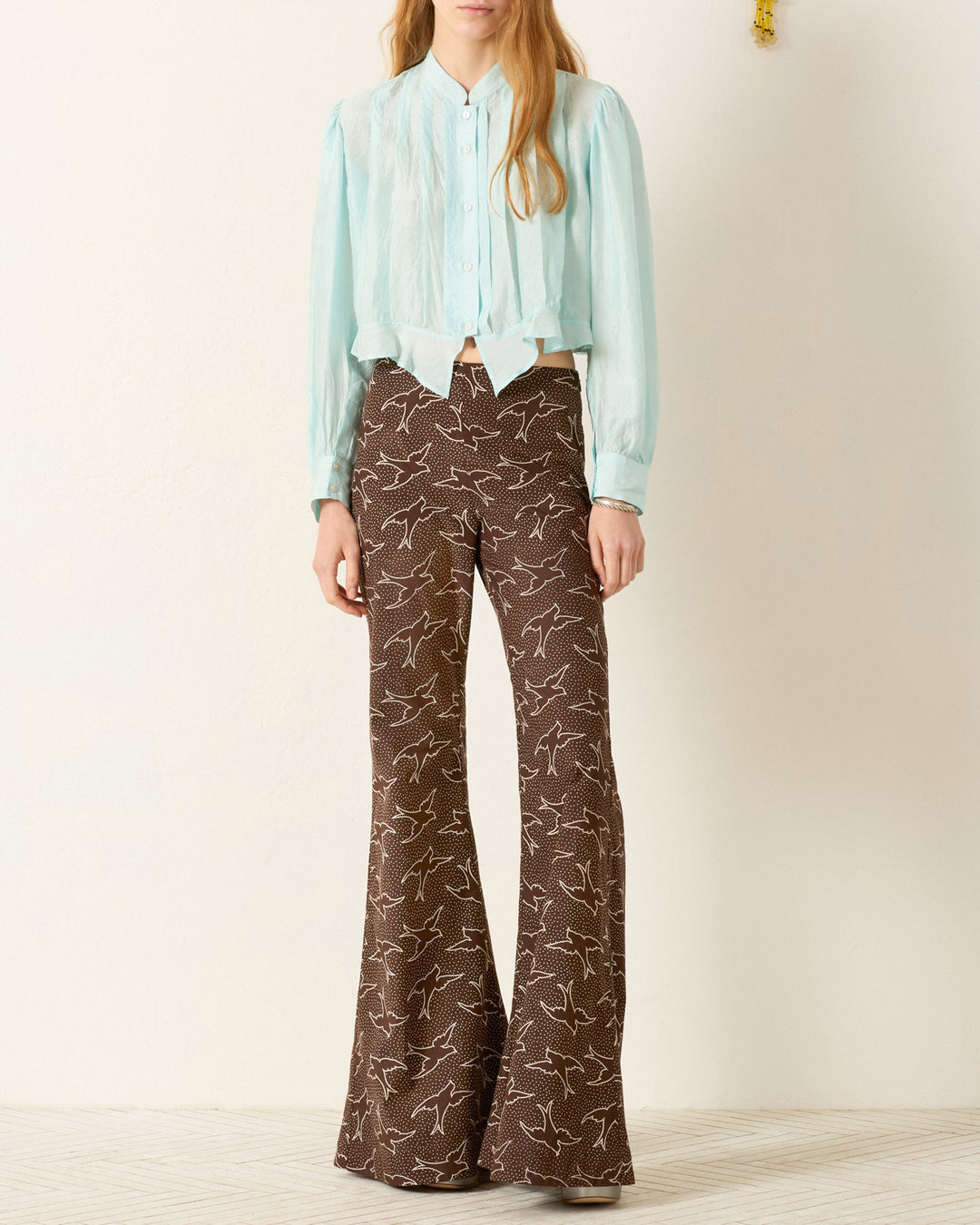 A person wearing the Ryland Morning Dew Silk Shirt and high-waisted brown flared pants with a white bird pattern stands against a plain background.