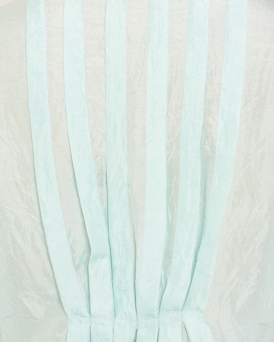 The Ryland Morning Dew Silk Shirt is a light blue sheer hand-loomed blouse featuring vertical pleats for texture and a delicate ruffled hem, creating an elegant look on a pale background.