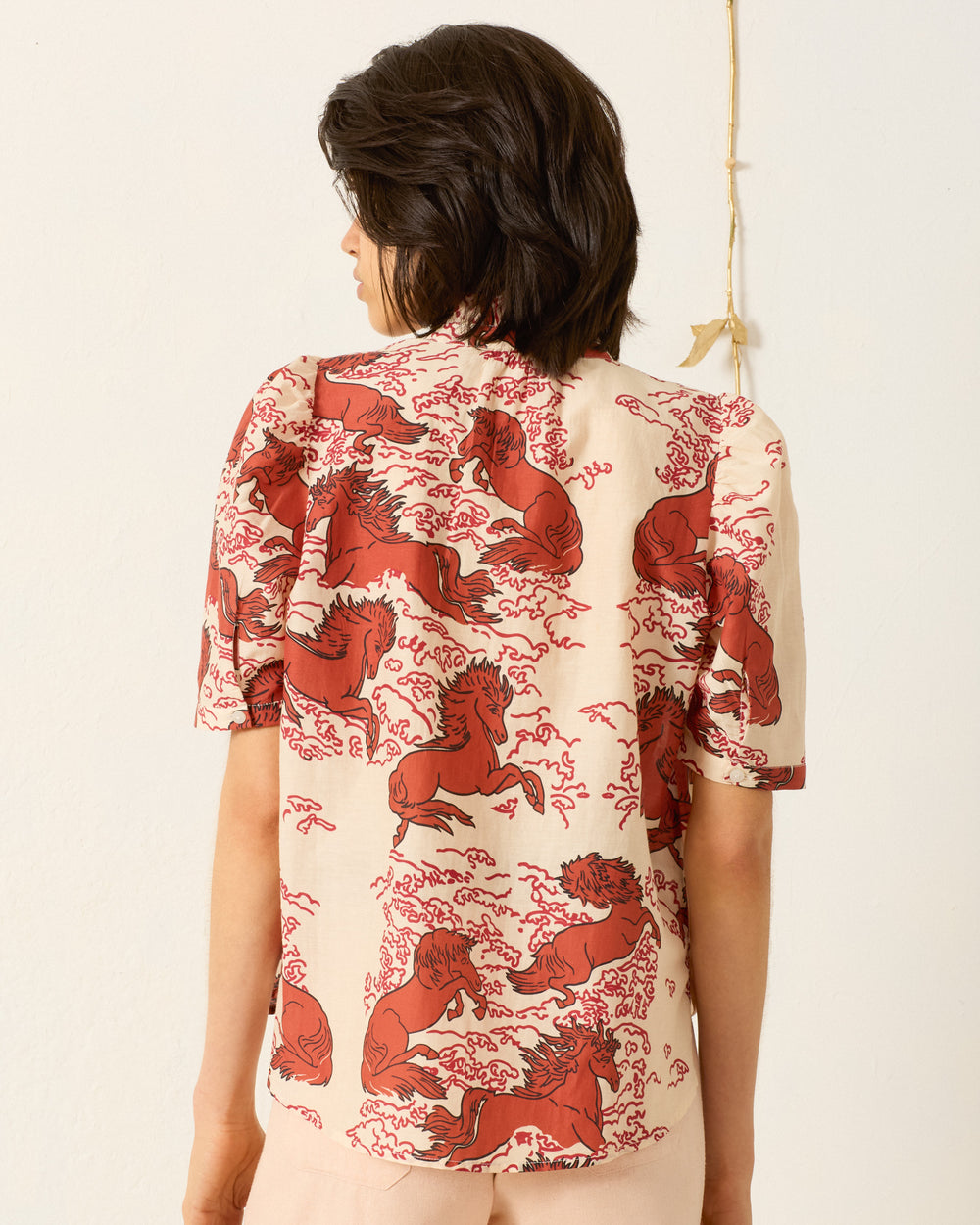 Person shown from behind, wearing the Winnie Rouge Pegasus Shirt—a cotton-silk shirt with a red horse print on a light background.