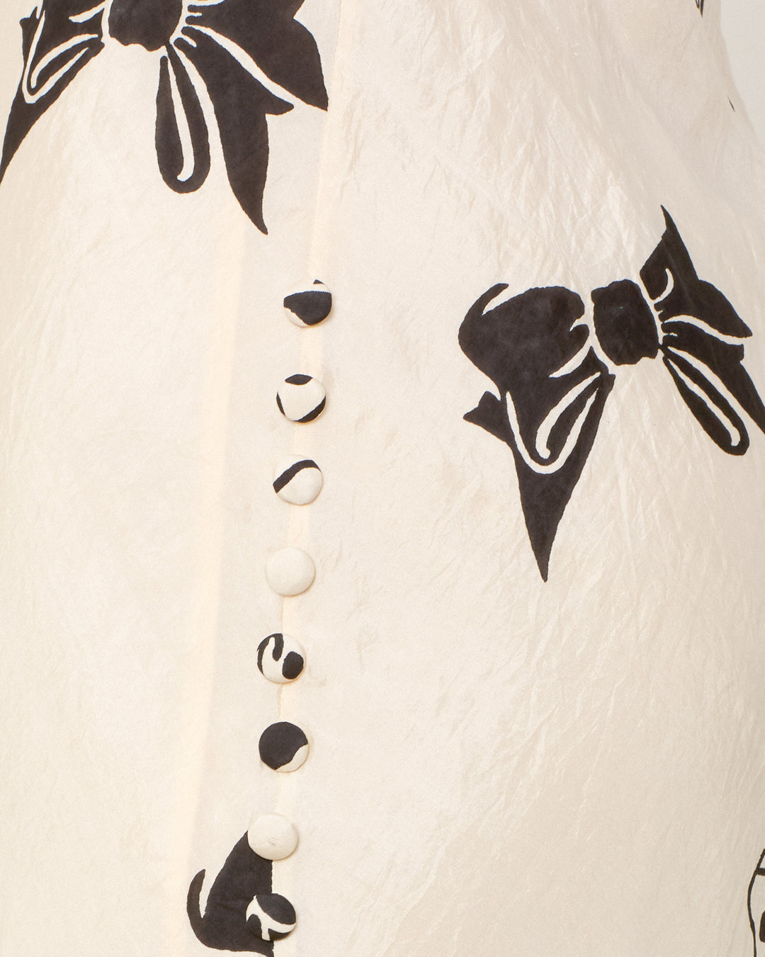 Close-up of white fabric adorned with black bow prints and a row of round buttons, some with partial black patterns, neatly sewn along a seam—an exquisite detail on the Adele Black Tie Silk Dress. This artisan garment is crafted from hand-loomed silk and thoughtfully hand-block-printed for a truly unique slip dress.