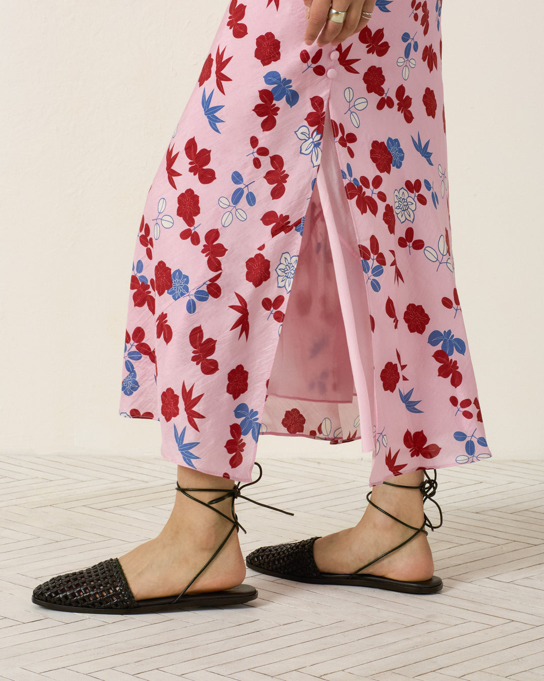 A person wearing the Adele Tutu Bloom Silk Dress and black woven lace-up sandals stands on a light tiled floor.