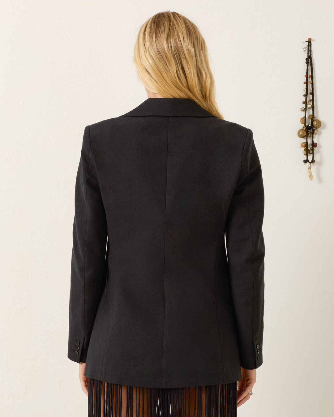 A person with long blonde hair, shown from the back, wears the Afternoon Pressed Daisy Blazer and stands near a wall adorned with hanging handmade daisy decorations.