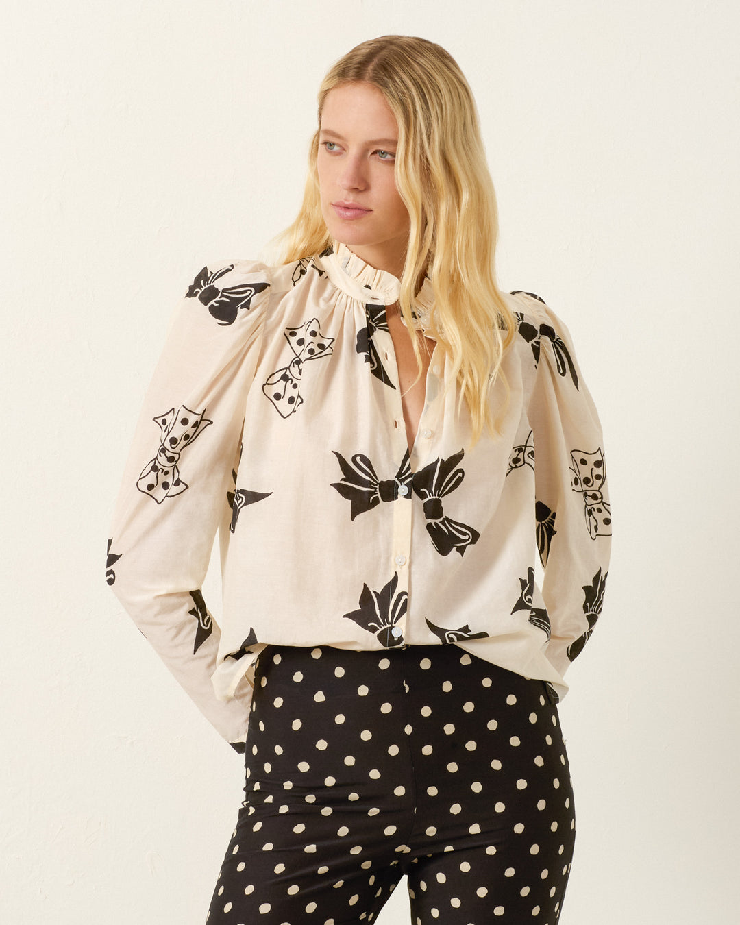 A woman with long blonde hair wears the Artemis Black Tie Shirt, featuring hand-block-printed black abstract patterns, paired with high-waisted black pants with white polka dots.