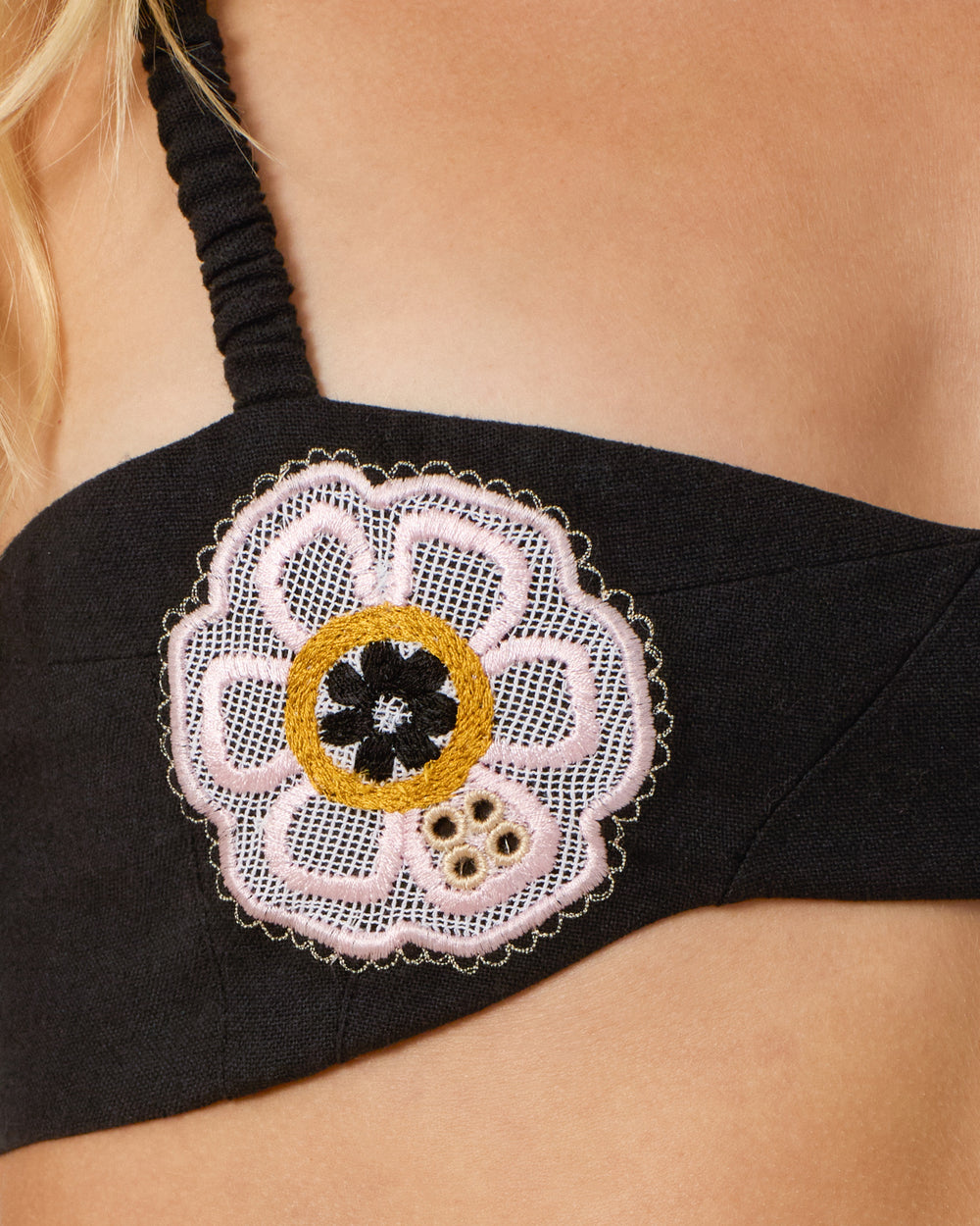 Close-up of the Avalon Pressed Daisy Bralette in black cotton, featuring a decorative embroidered flower patch in pink, gold, black, and white with handmade daisies and delicate adjustable ties.